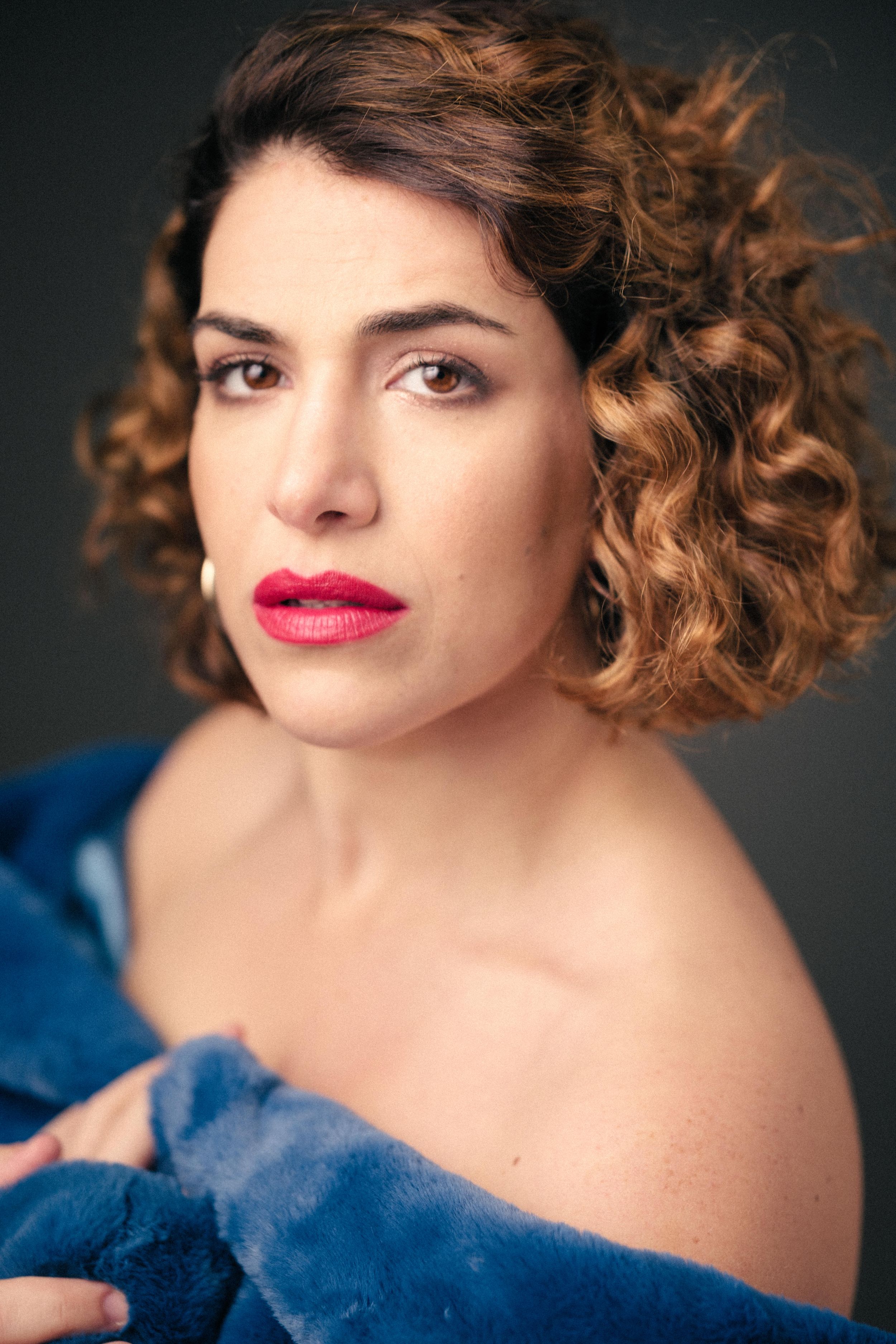 Studio portrait with red lipstick and off-shoulder blue fur coat.