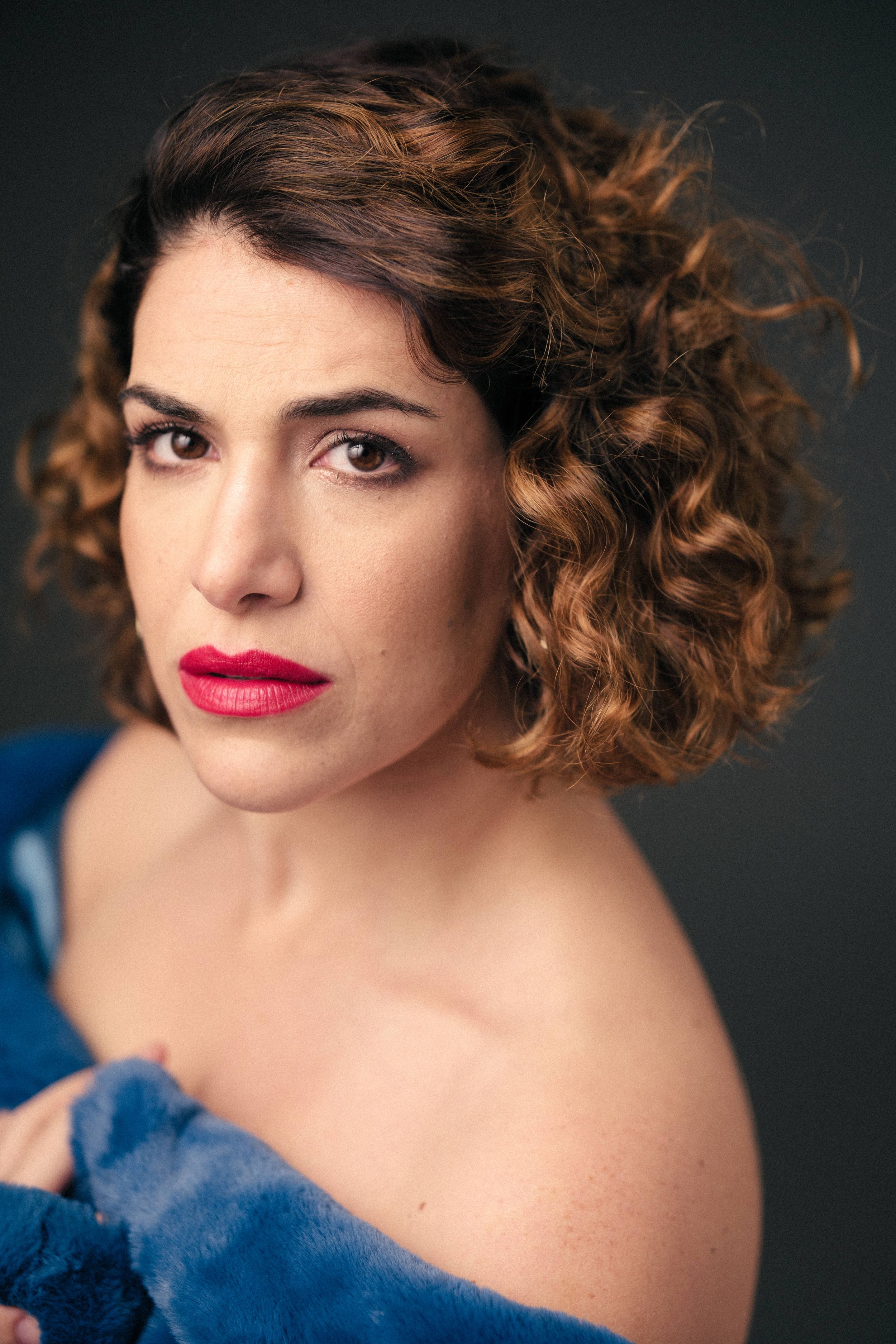 Elegant headshot with curled hair and bright makeup against dark background.