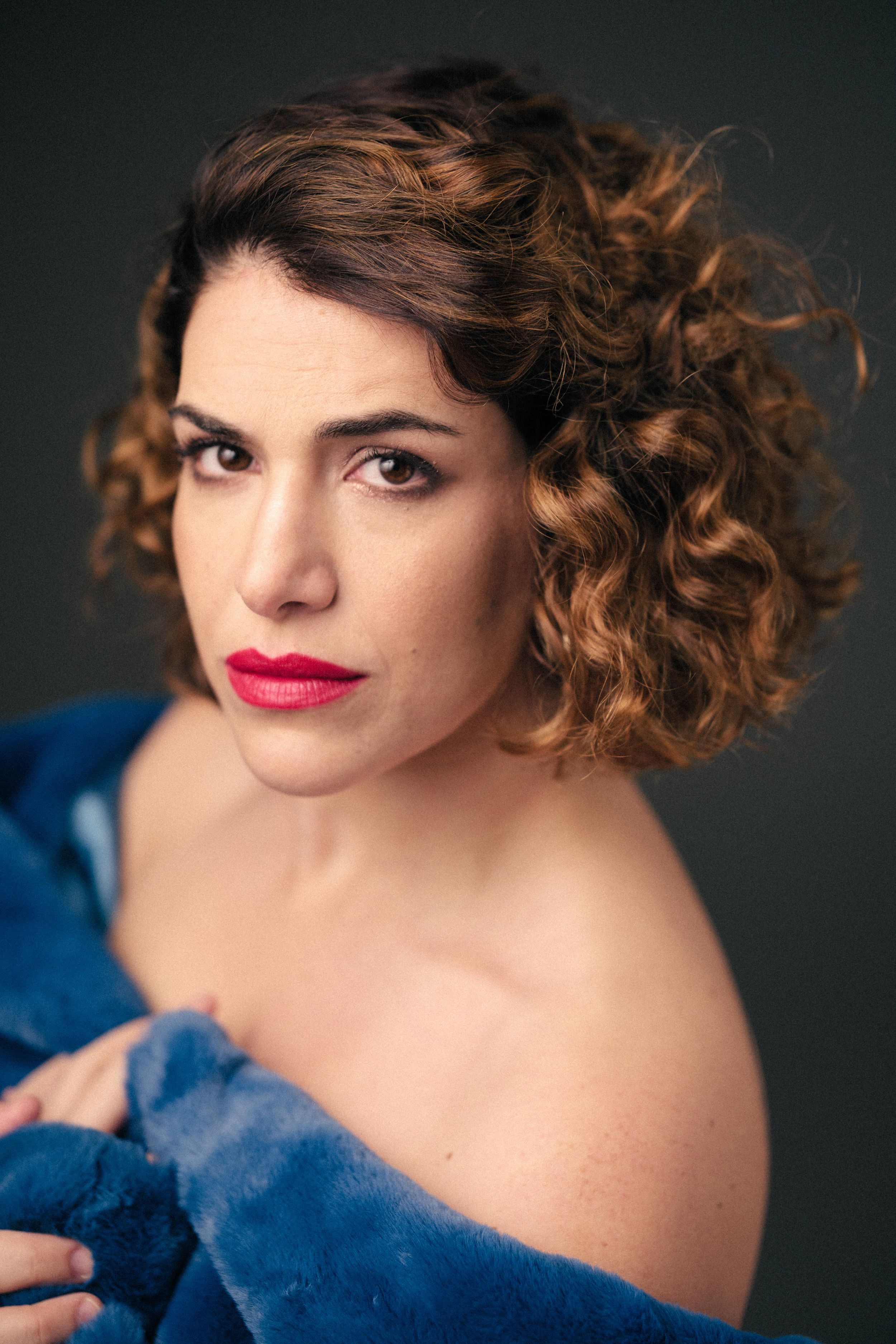 Glamour portrait featuring curly hair, bright red lipstick, and a blue garment against a dark background.