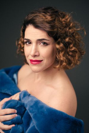 Artistic portrait with curly hair and bright red lipstick against dark backdrop wearing blue.