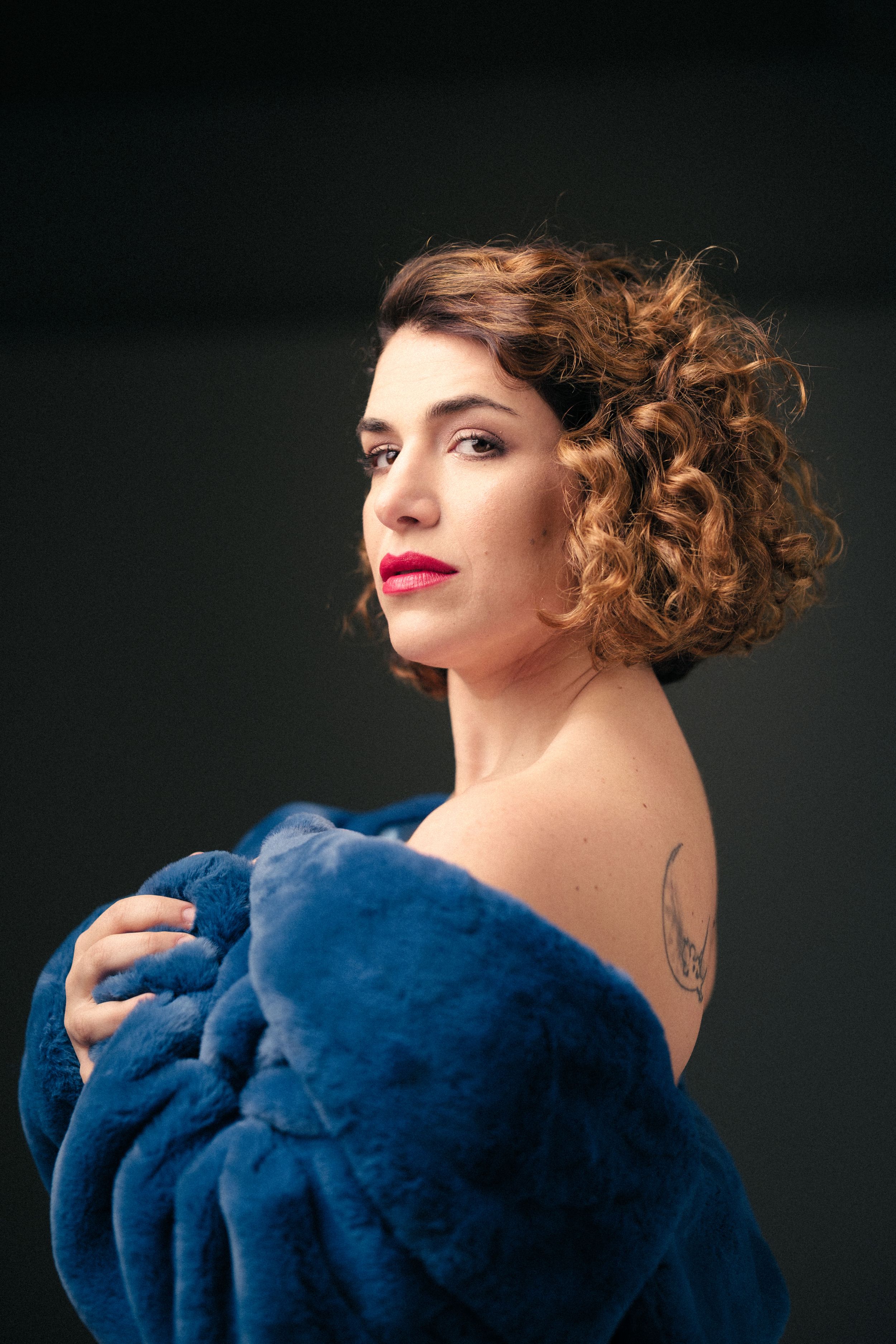 Side profile portrait showcasing curly hair and a plush blue wrap against dark background.