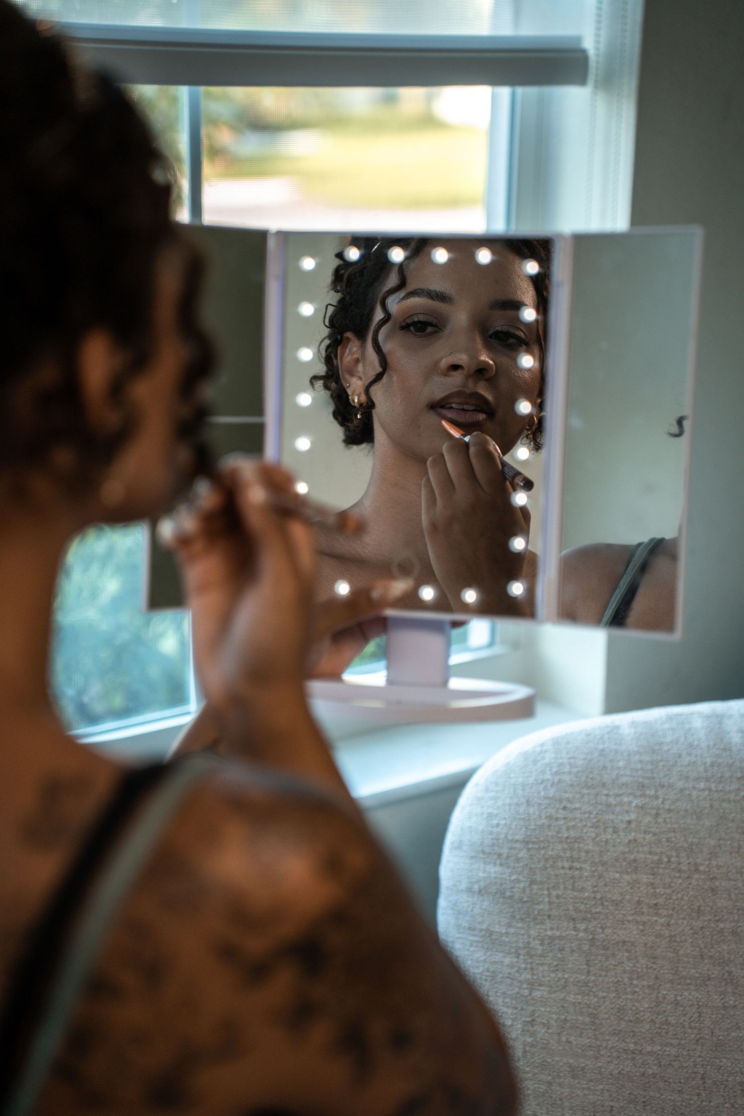 Person applying eye makeup in vanity mirror reflection with professional lighting setup in makeup studio.