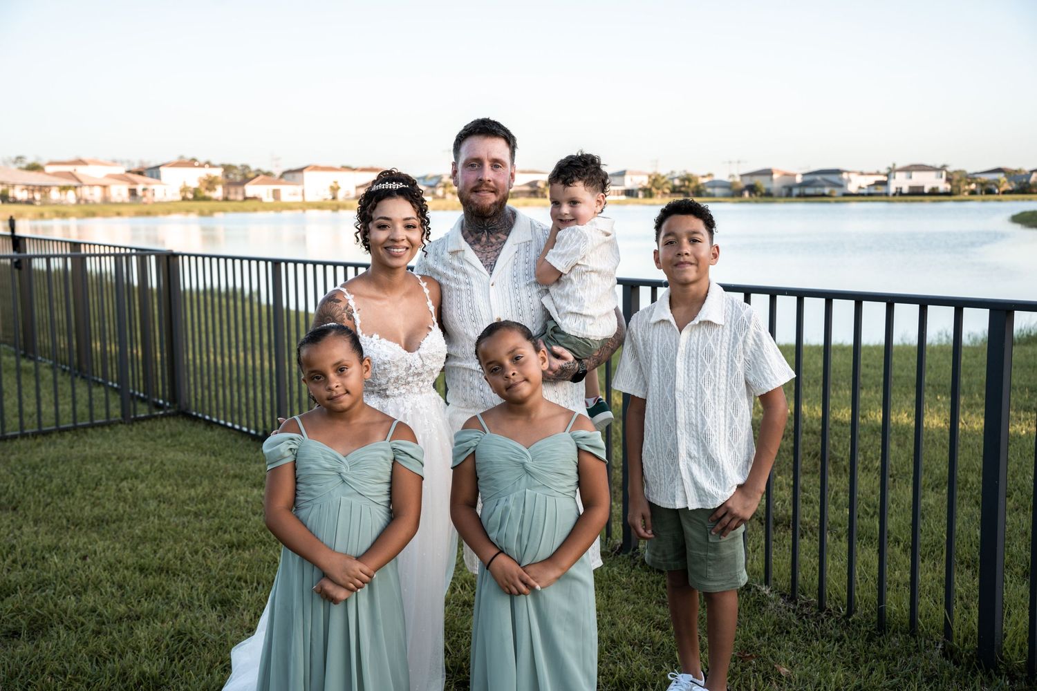 Wedding party in mint green dresses and suits pose outdoors by a waterfront on a sunny afternoon.