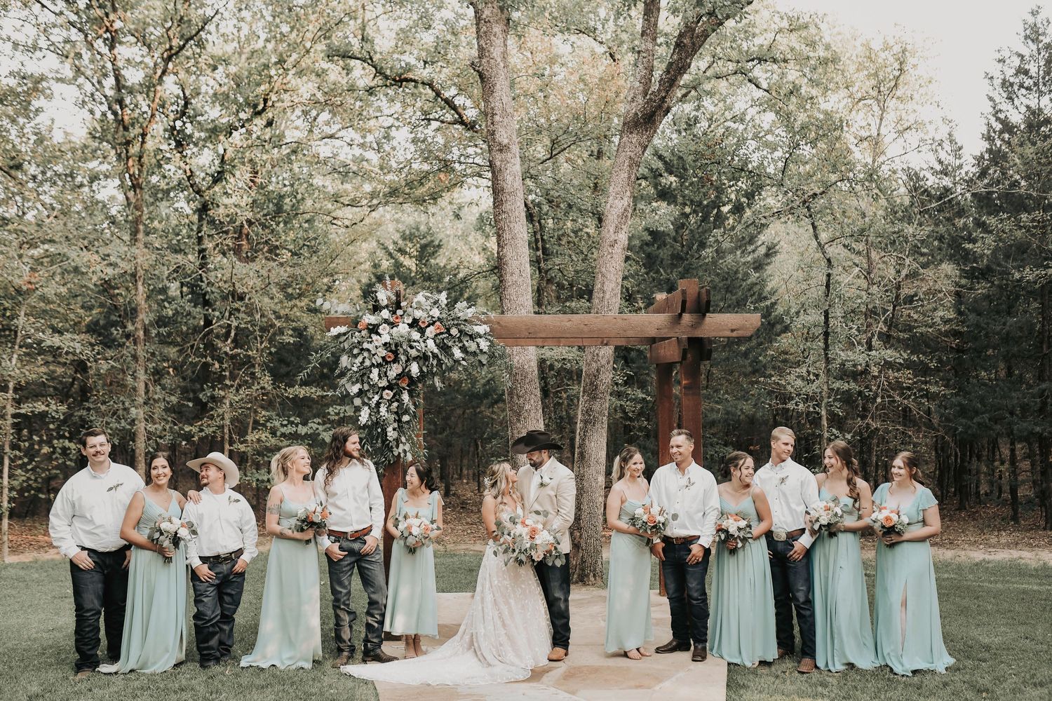 Full wedding party lined up in front of modern rustic barn at Whispering Oaks