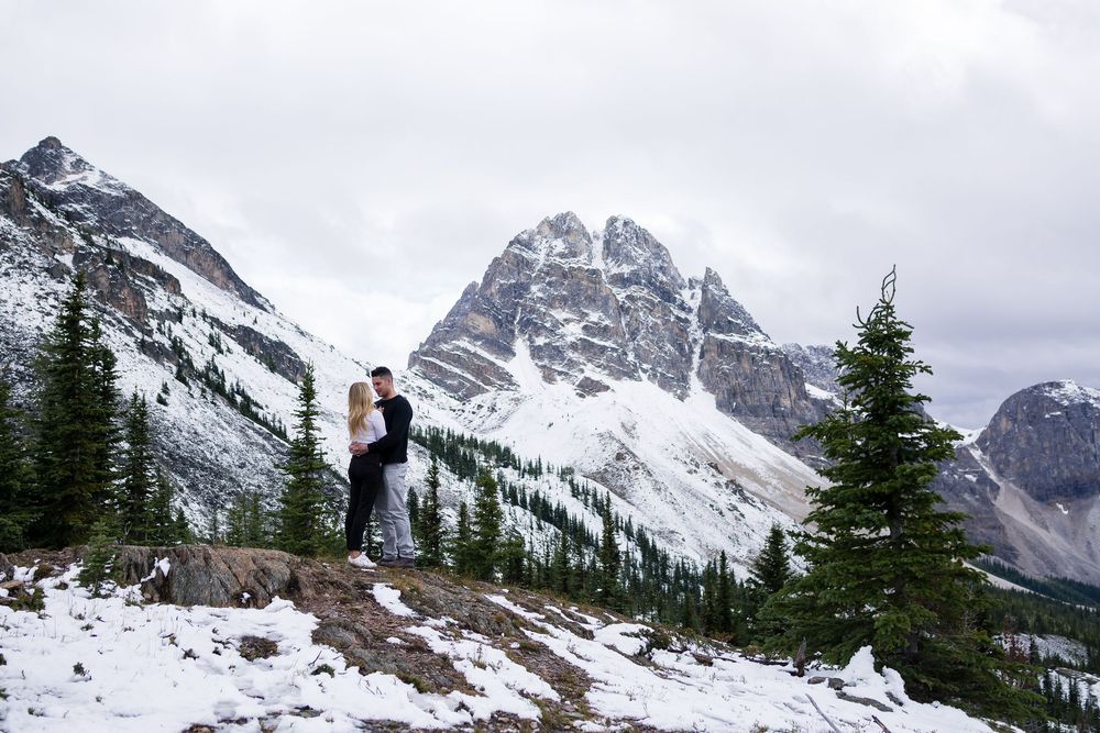 Snowy mountain landscape with evergreen trees dotting the slopes beneath dramatic rocky peaks in winter.