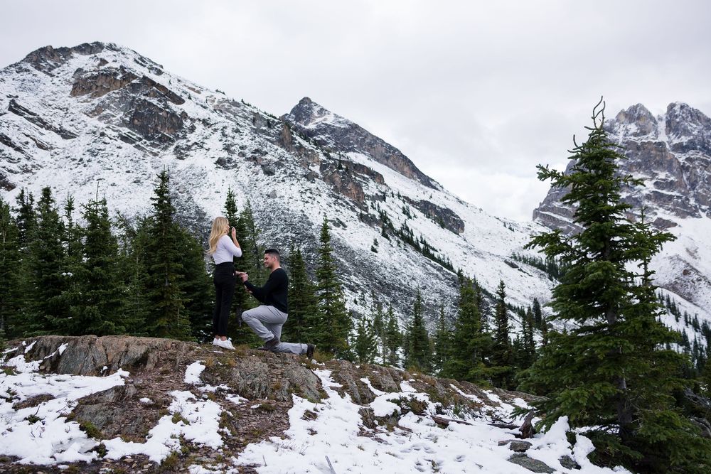 Snow-capped mountain peaks and evergreen trees create a dramatic winter landscape in rugged alpine terrain.