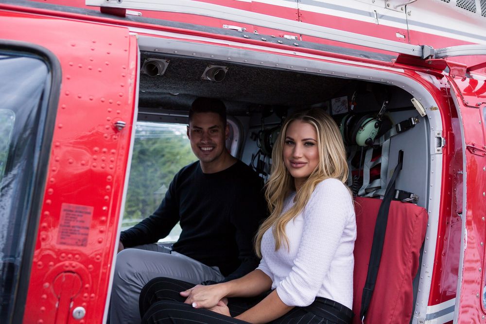 Two passengers smile inside a red helicopter cockpit during a scenic flight.