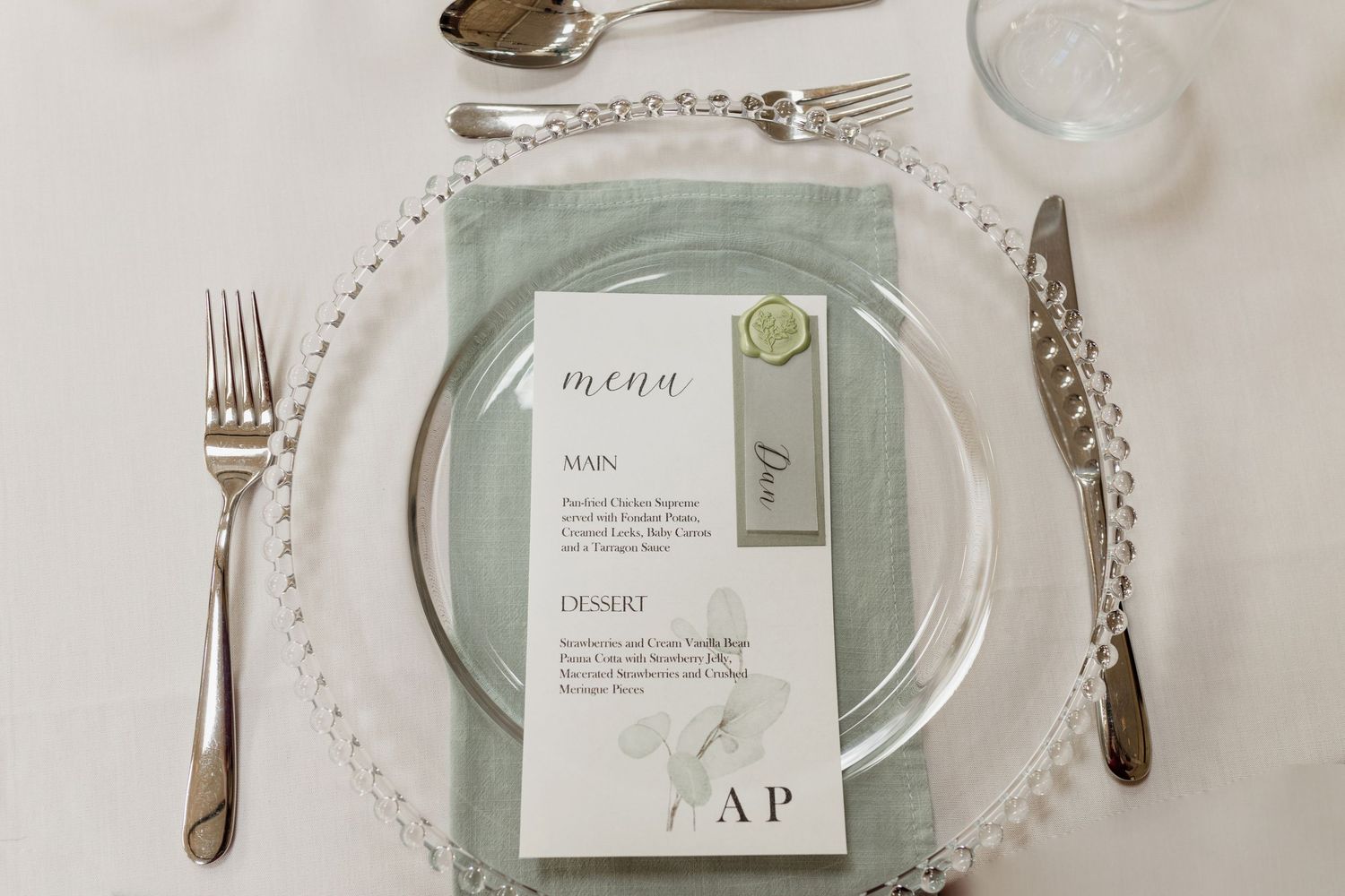 Elegant table setting with silver flatware, vintage plates, and menu cards in soft sage green and white tones.