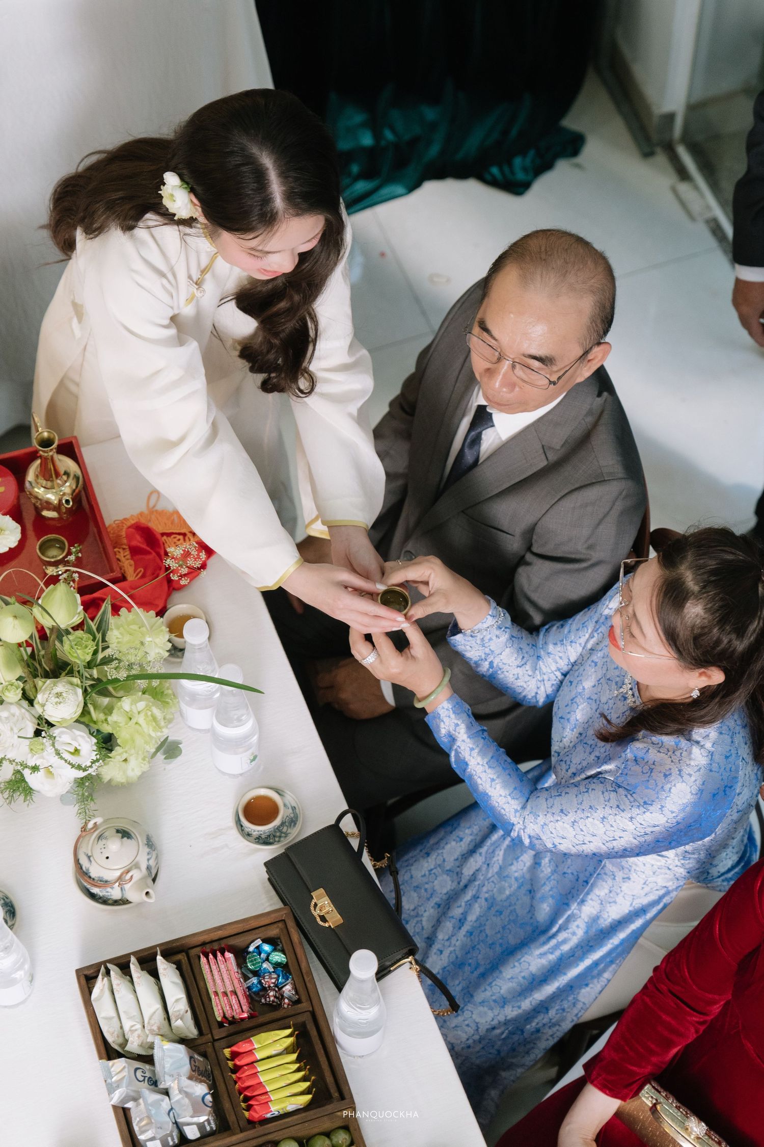 Overhead view of bride receiving jewelry from parents at traditional Vietnamese engagement ceremony table.