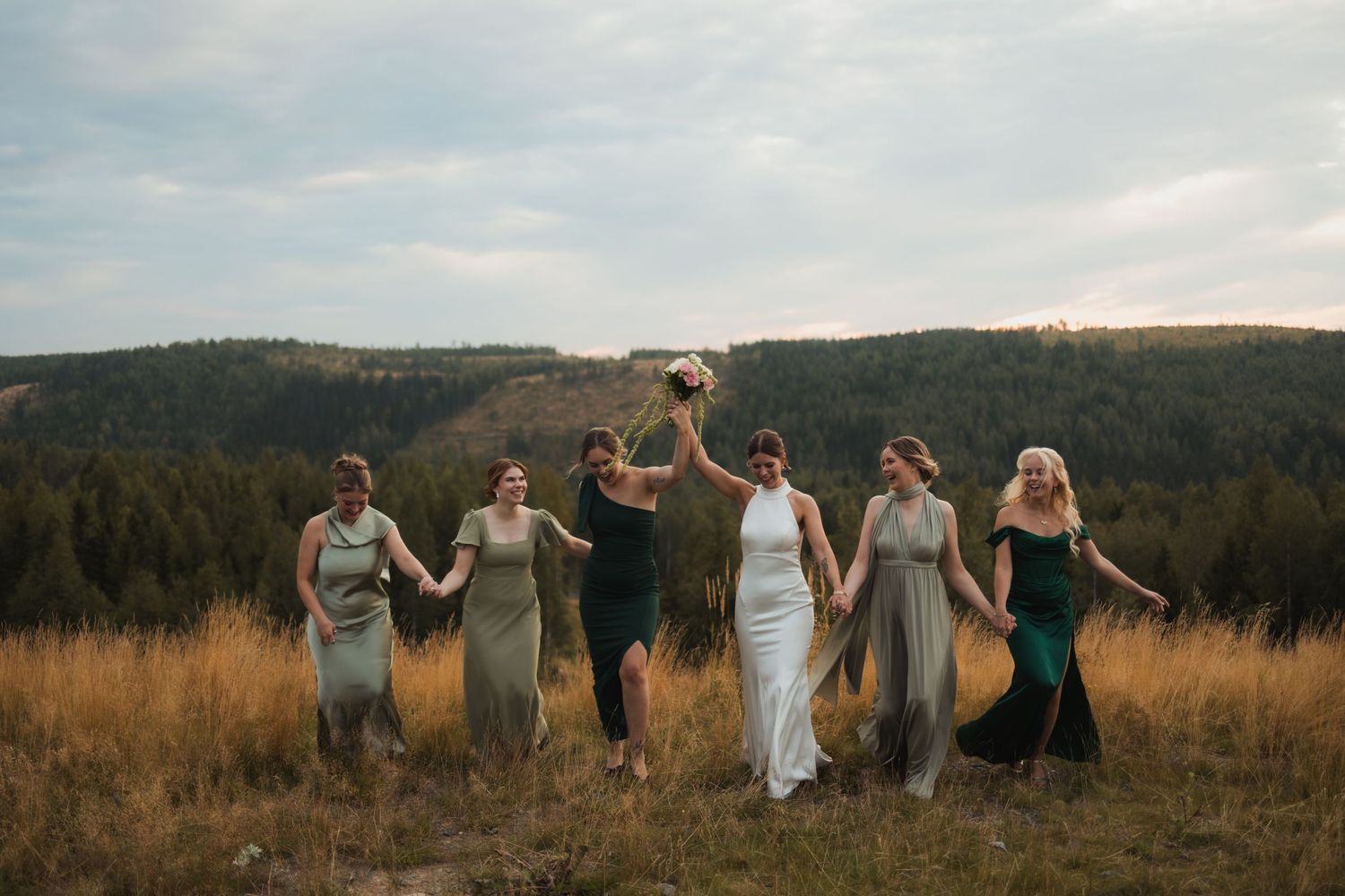 Wedding party walking together through a golden field with mountain views at sunset.