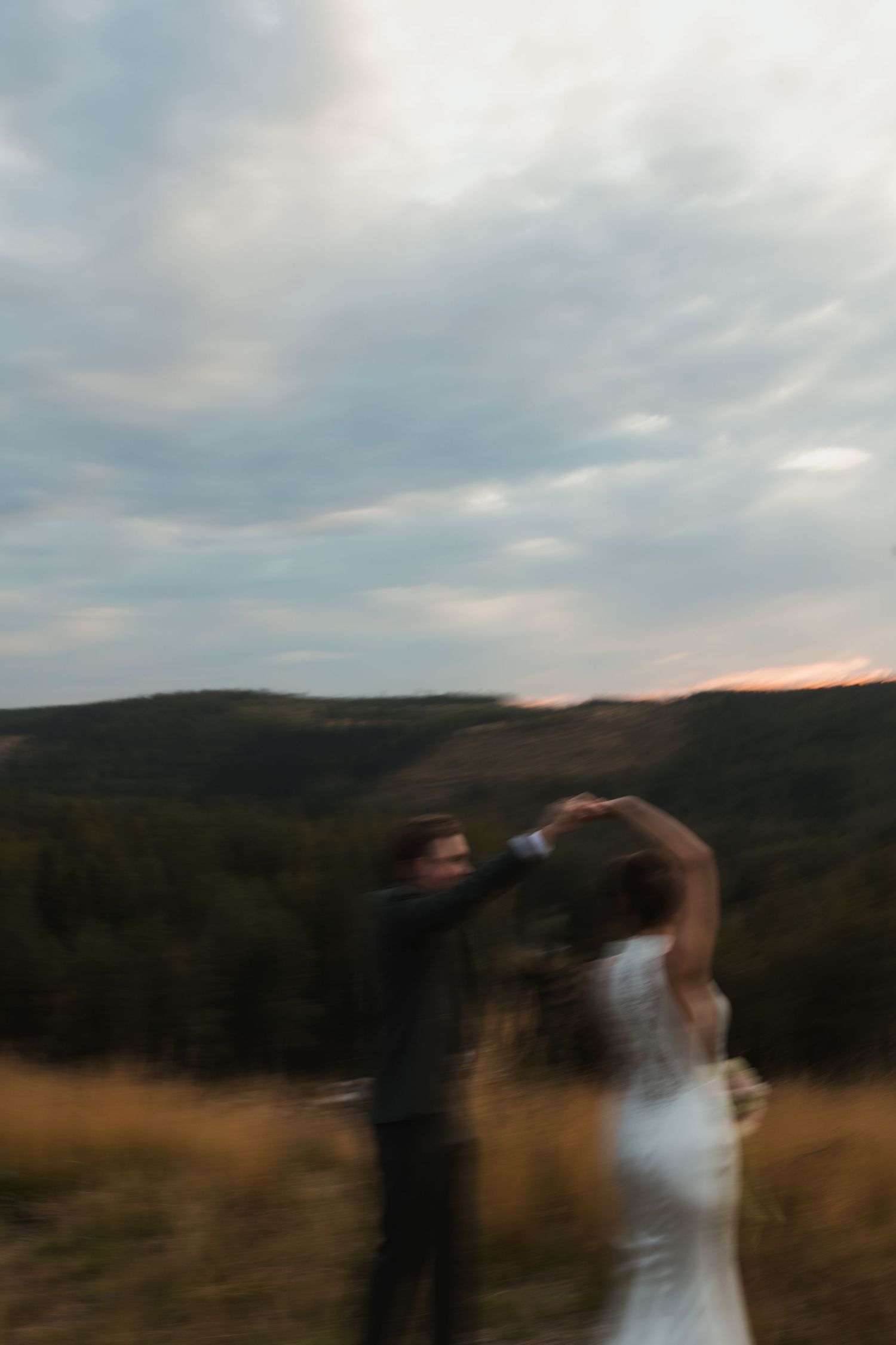A couple dancing in a field at sunset with mountains in the background.