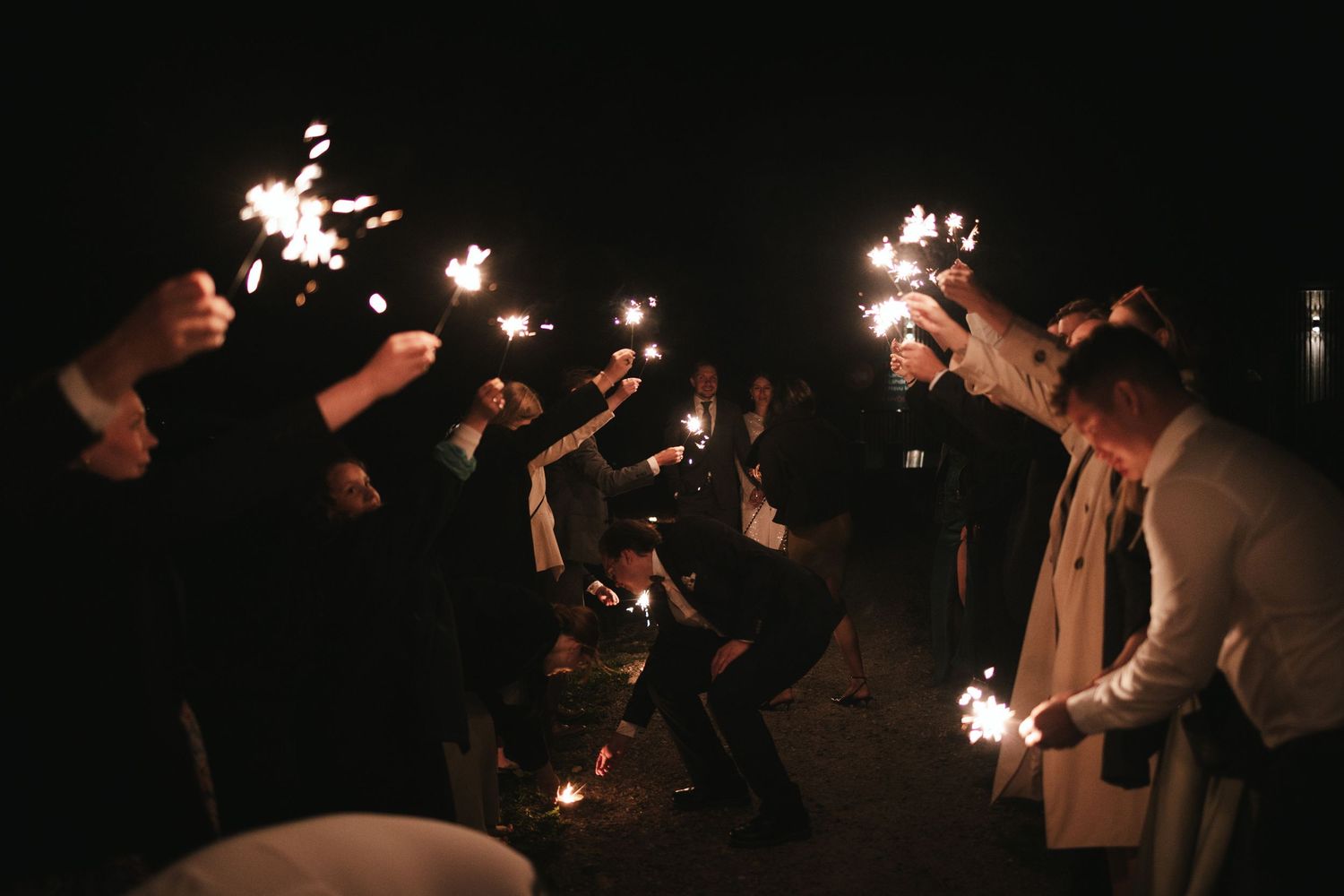 Wedding guests holding sparklers in the dark creating trails of light.