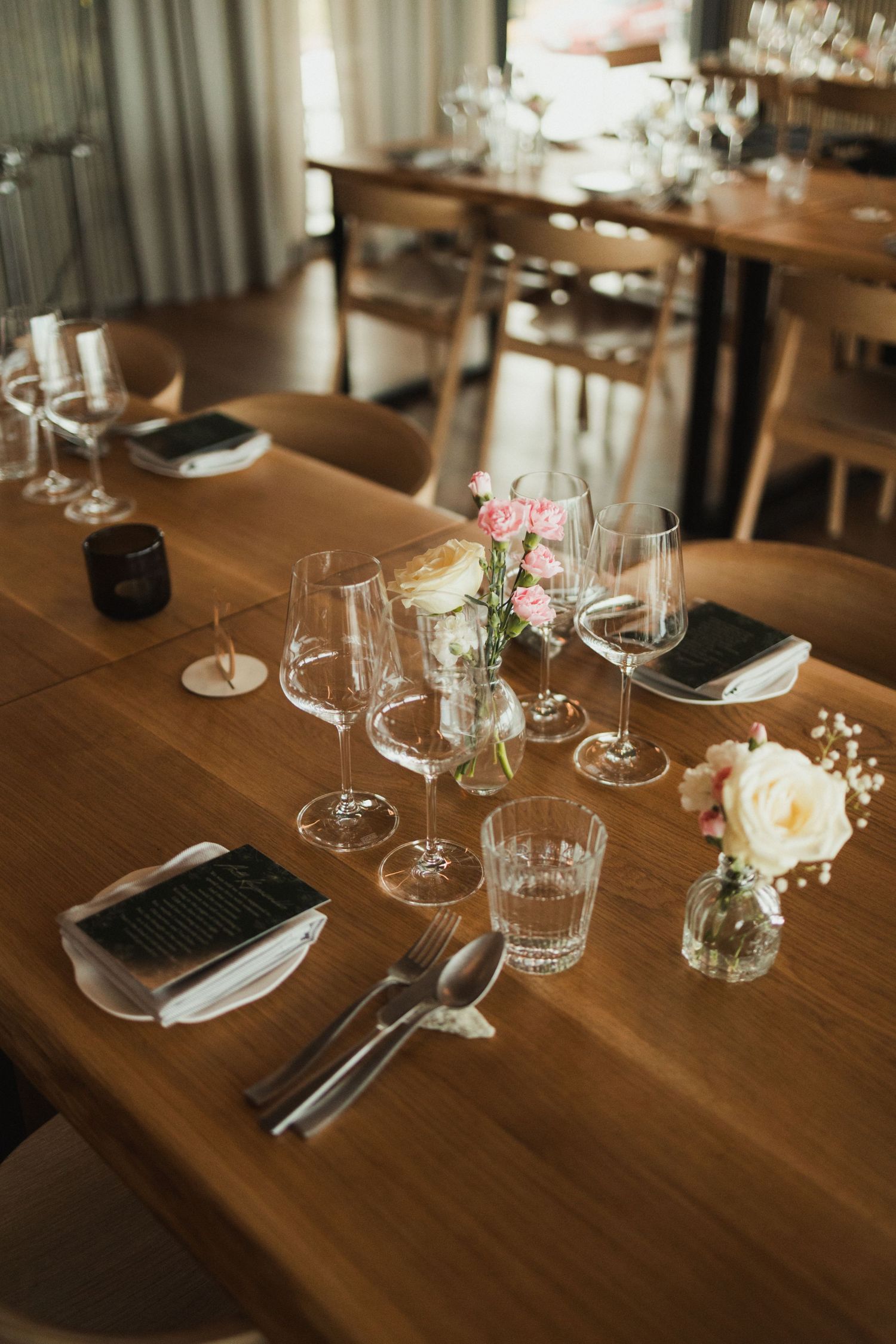Elegant table setting with wine glasses, pink roses, and place settings on a wooden dining table.