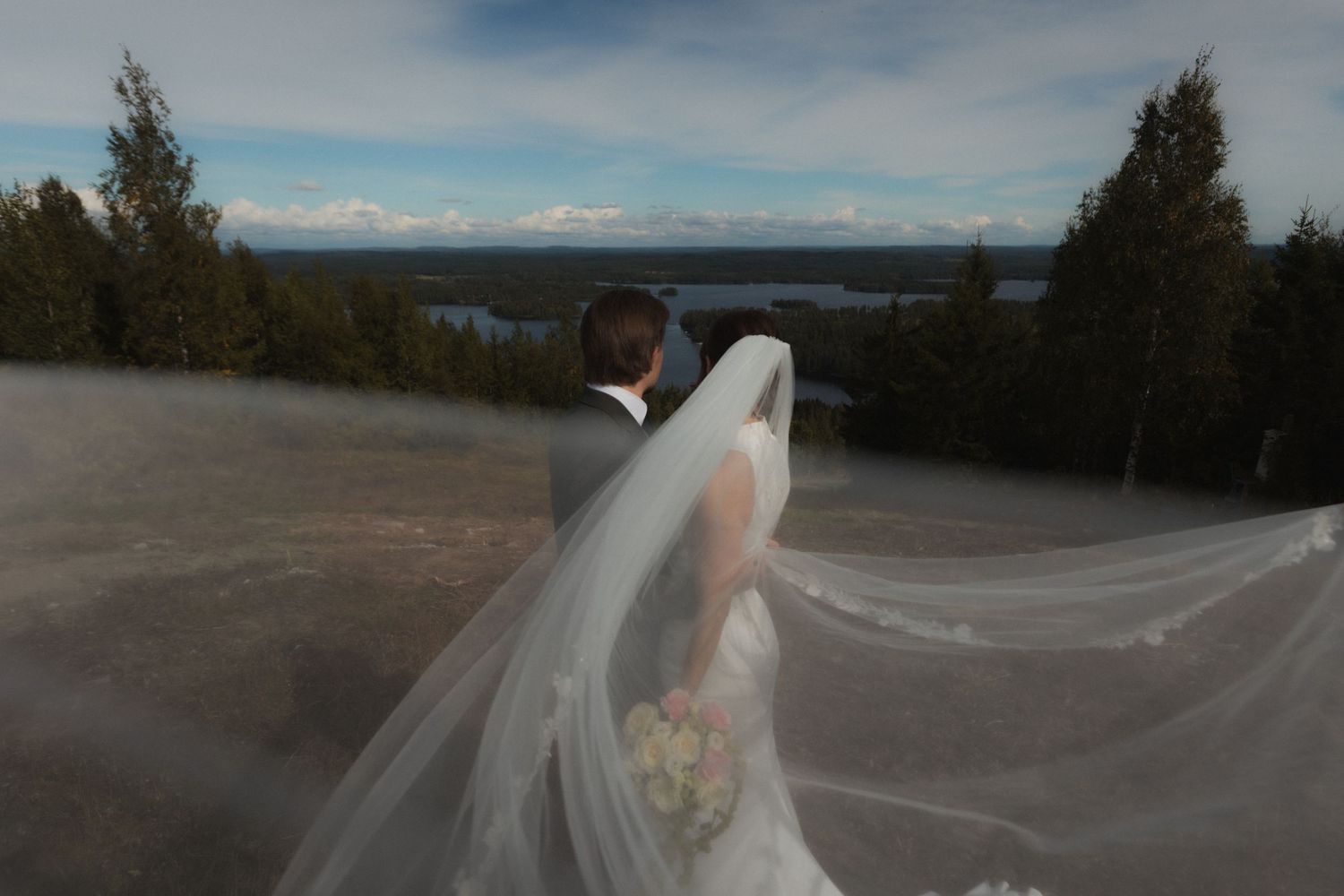 A flowing white wedding dress and veil caught in the breeze against a scenic landscape.