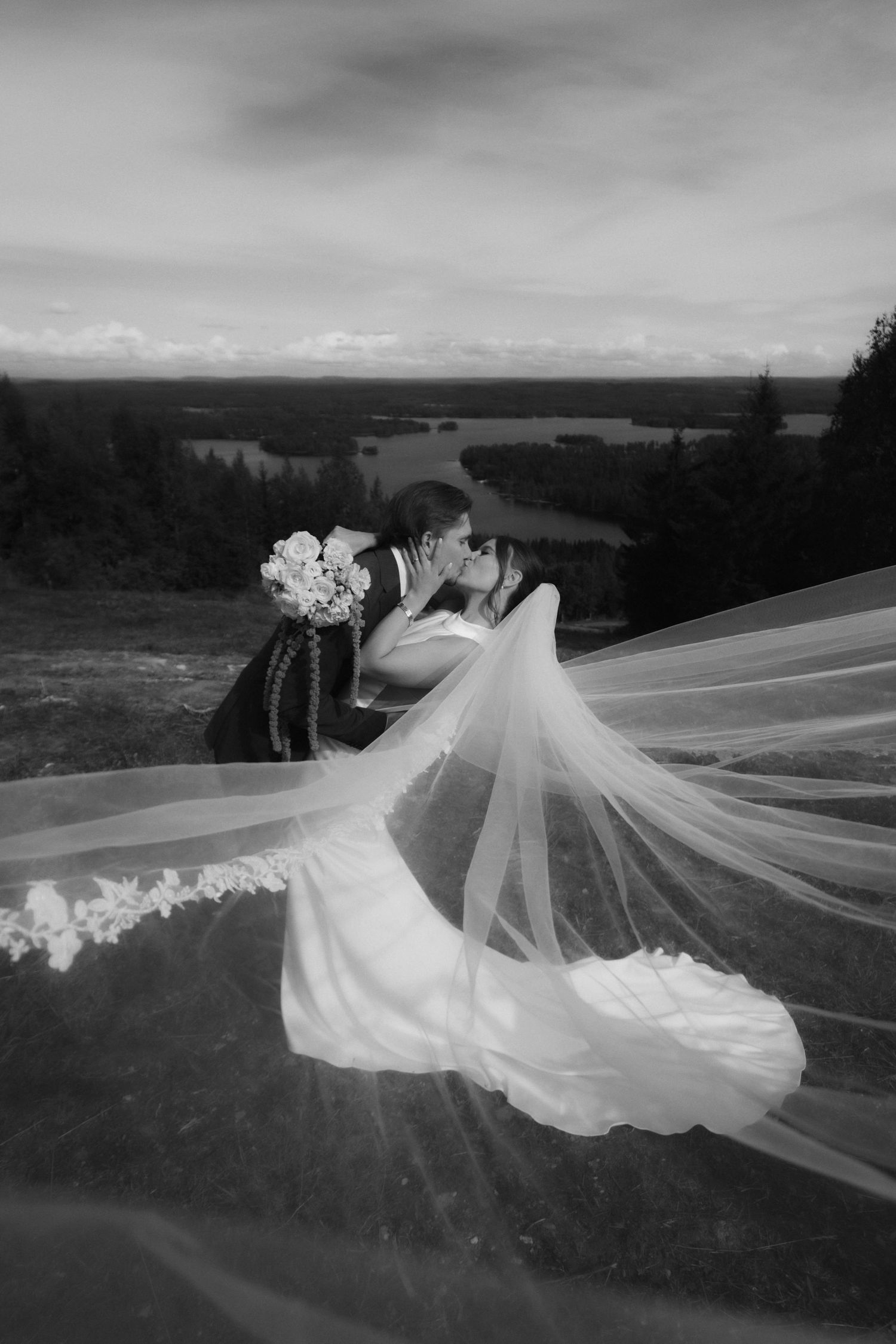 A dramatic black and white photo of a wedding dress and veil flowing in the wind on a hilltop.