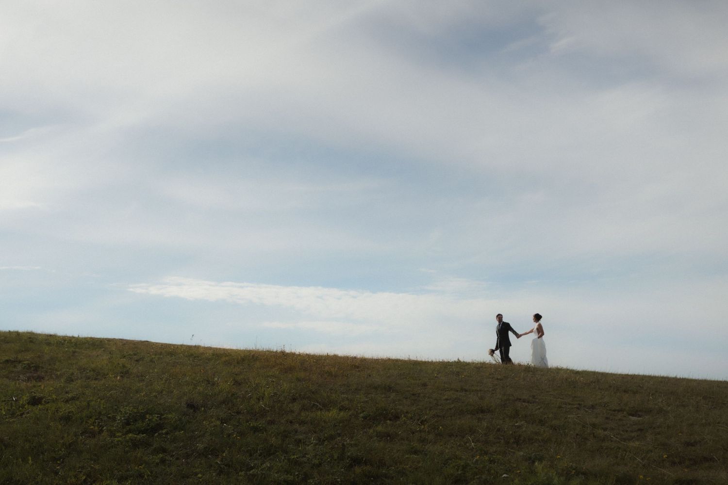 Silhouettes on a hilltop against a blue sky during a wedding photoshoot.