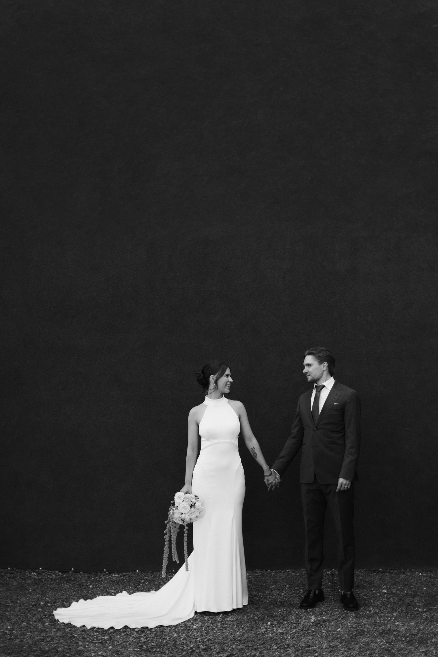 A black and white wedding portrait showing elegant dress details against a dark background.