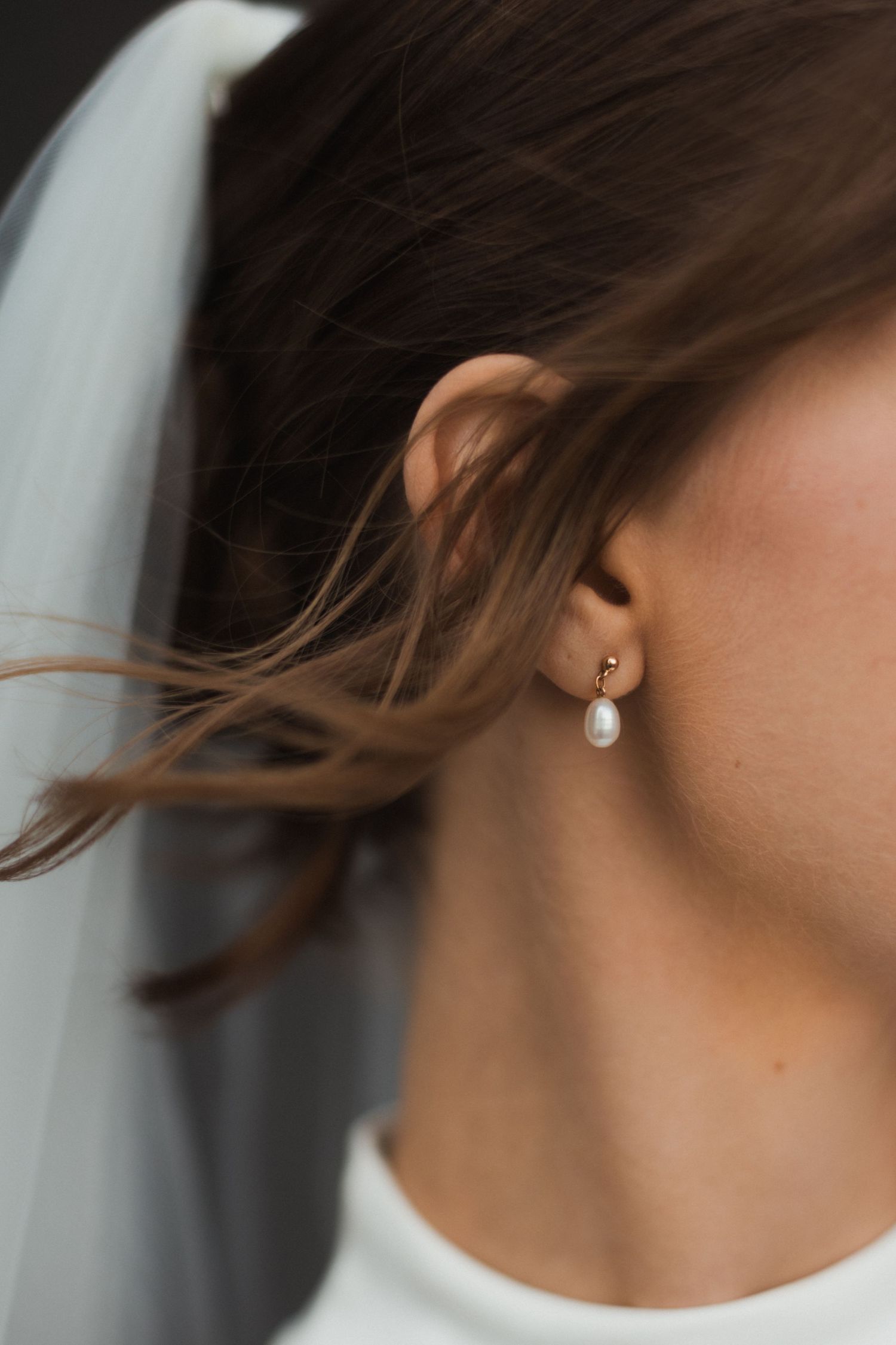 Close-up detail of an elegant pearl drop earring with a wedding veil in soft focus.