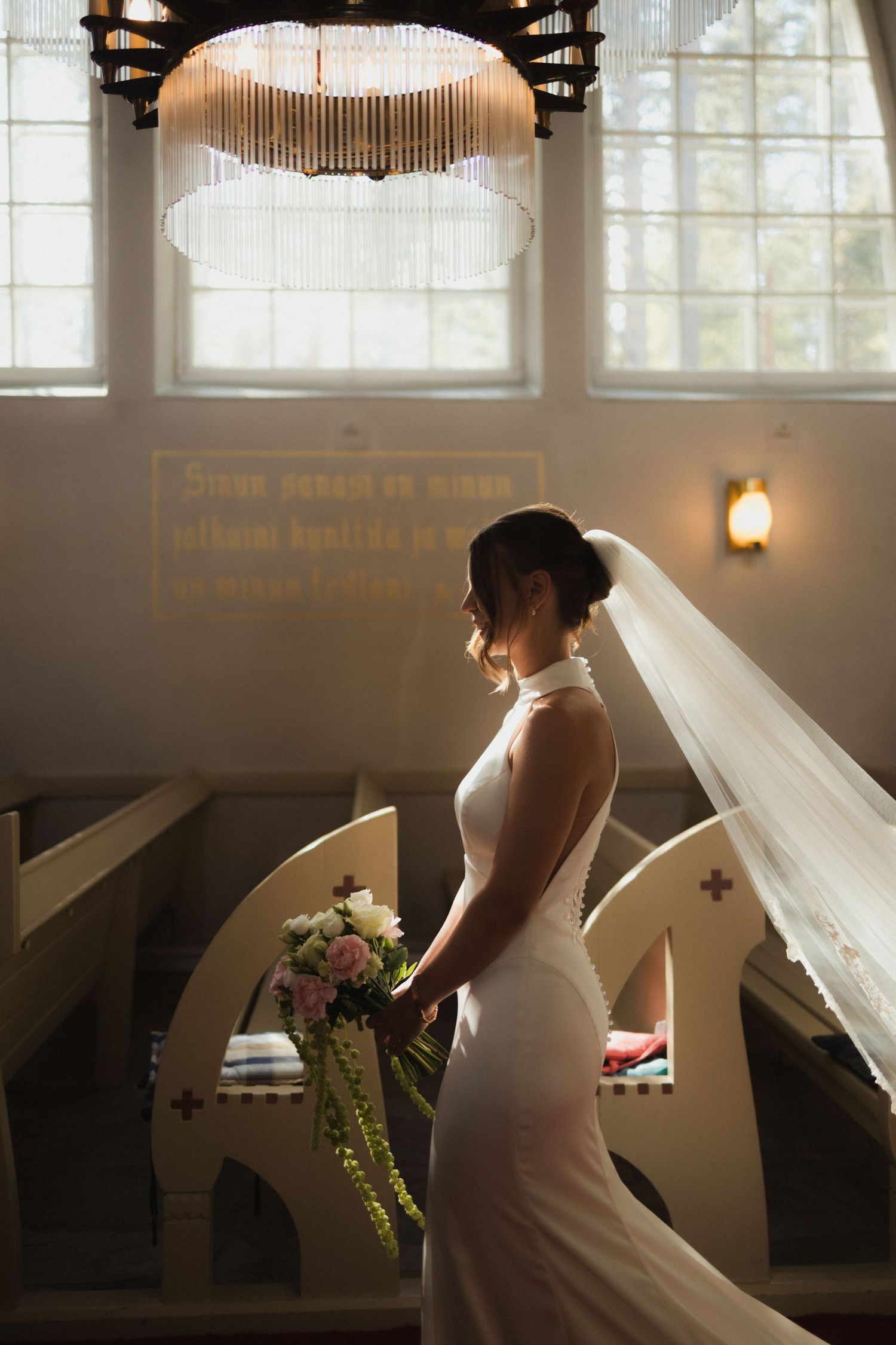 Elegant bridal portrait in a sunlit church interior with dramatic window light and flowing veil.