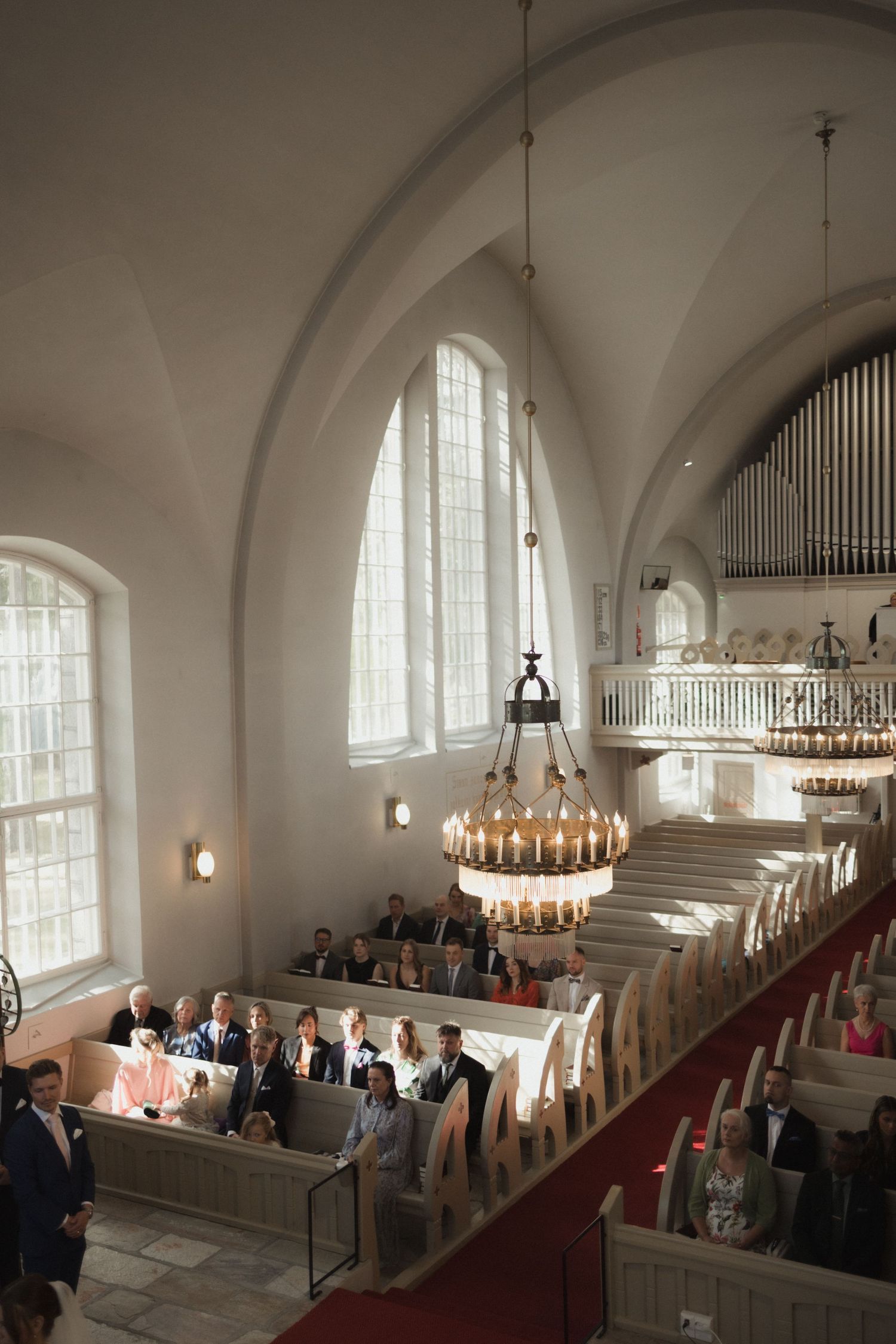 Church interior with arched windows and wooden pews filled with wedding guests.