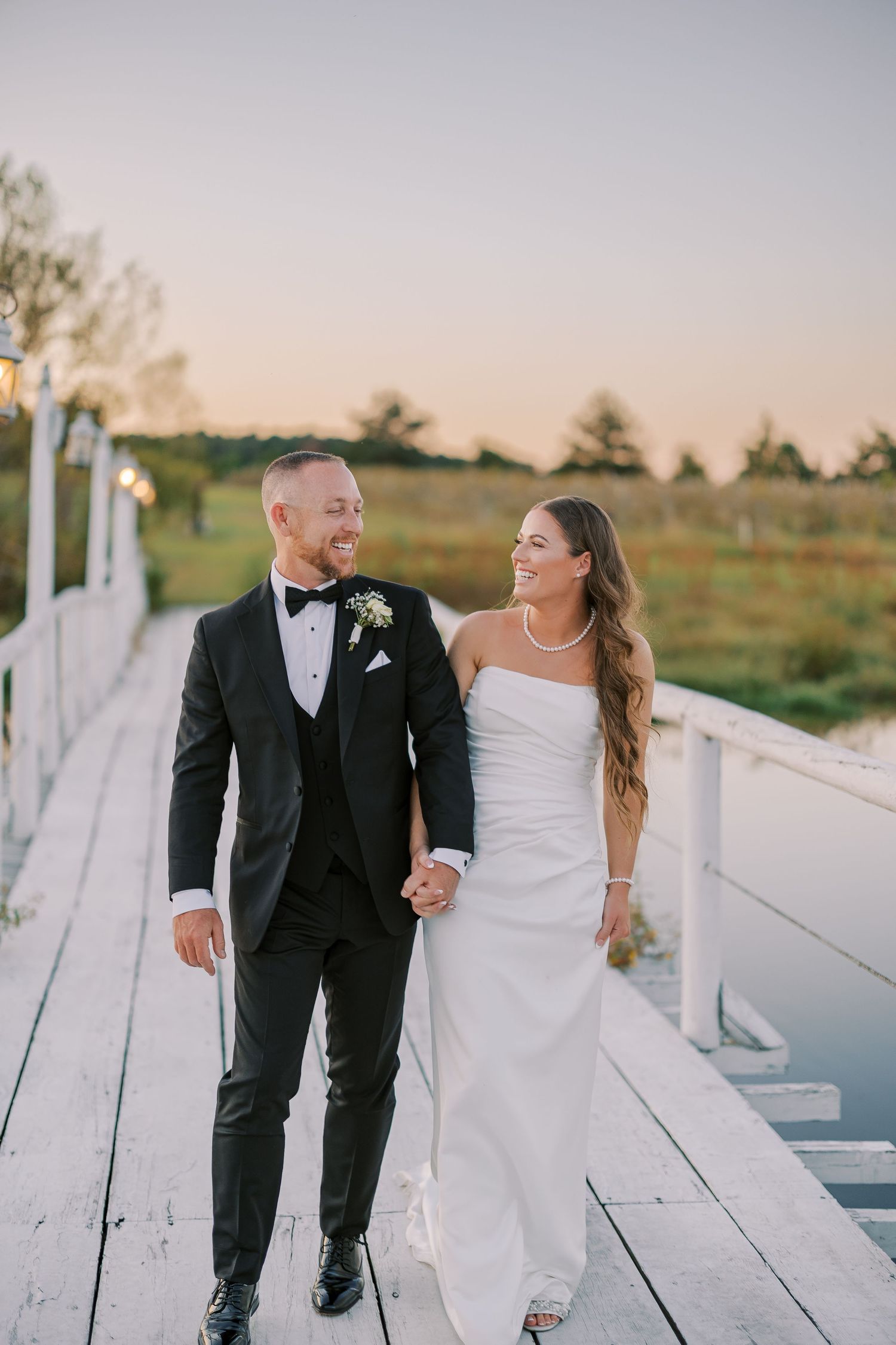 A couple shares candid laughter while walking on a wooden dock during their wedding photoshoot.