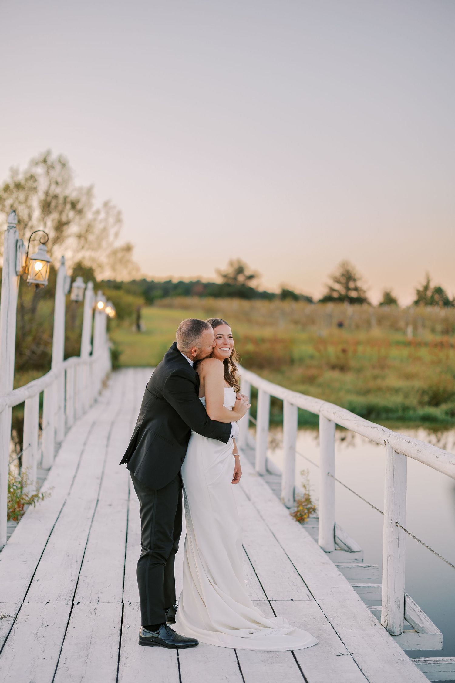 Romantic sunset wedding photos taken on a white wooden dock over water.