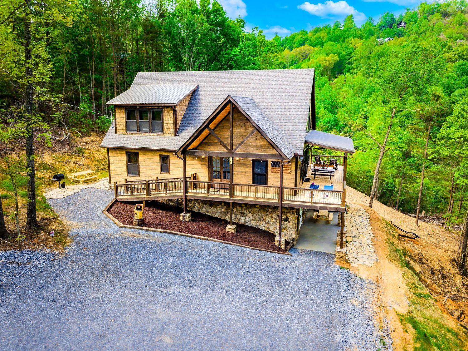 Aerial panoramic view of rustic wooden cabins nestled in lush green forest with winding gravel paths and parking areas.