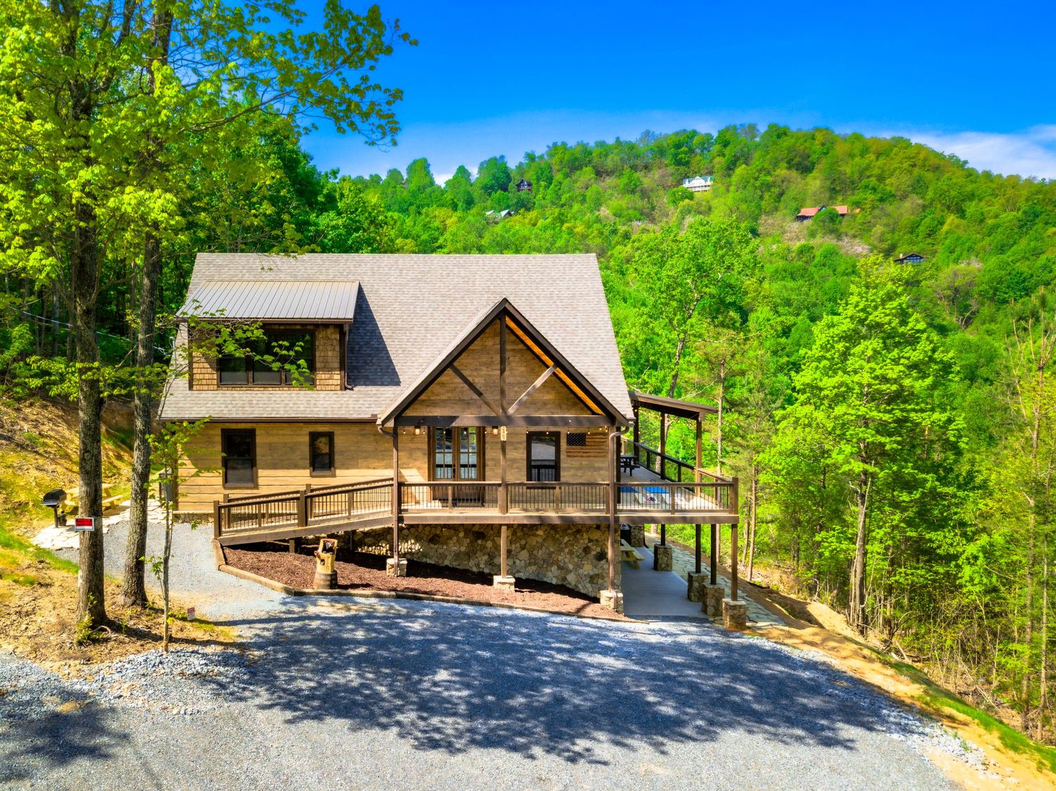 Scenic mountain cabin with stone and wood exterior nestled among lush green trees on a sunny summer day.