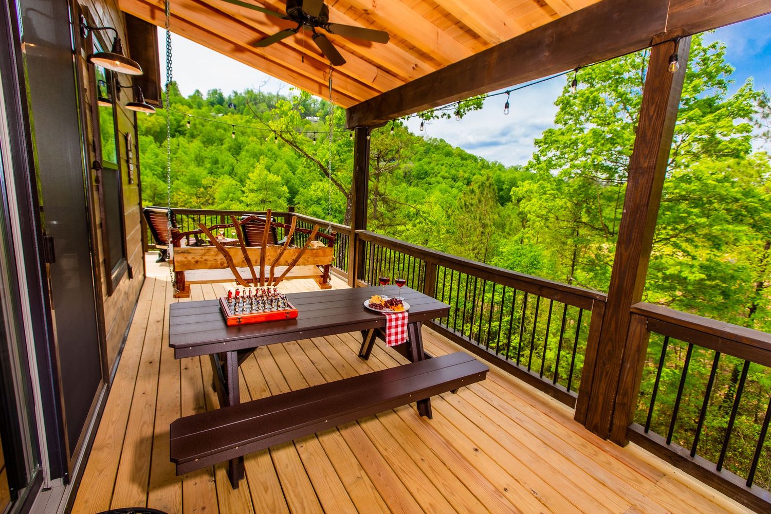 Spacious wooden deck with railing overlooking lush green forest views and comfortable outdoor seating arrangements.
