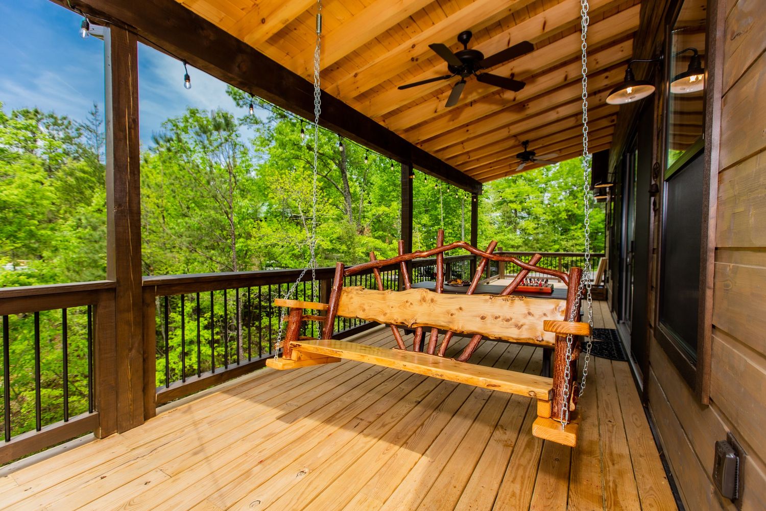 Covered wooden deck with ceiling fans overlooking lush forest landscape.