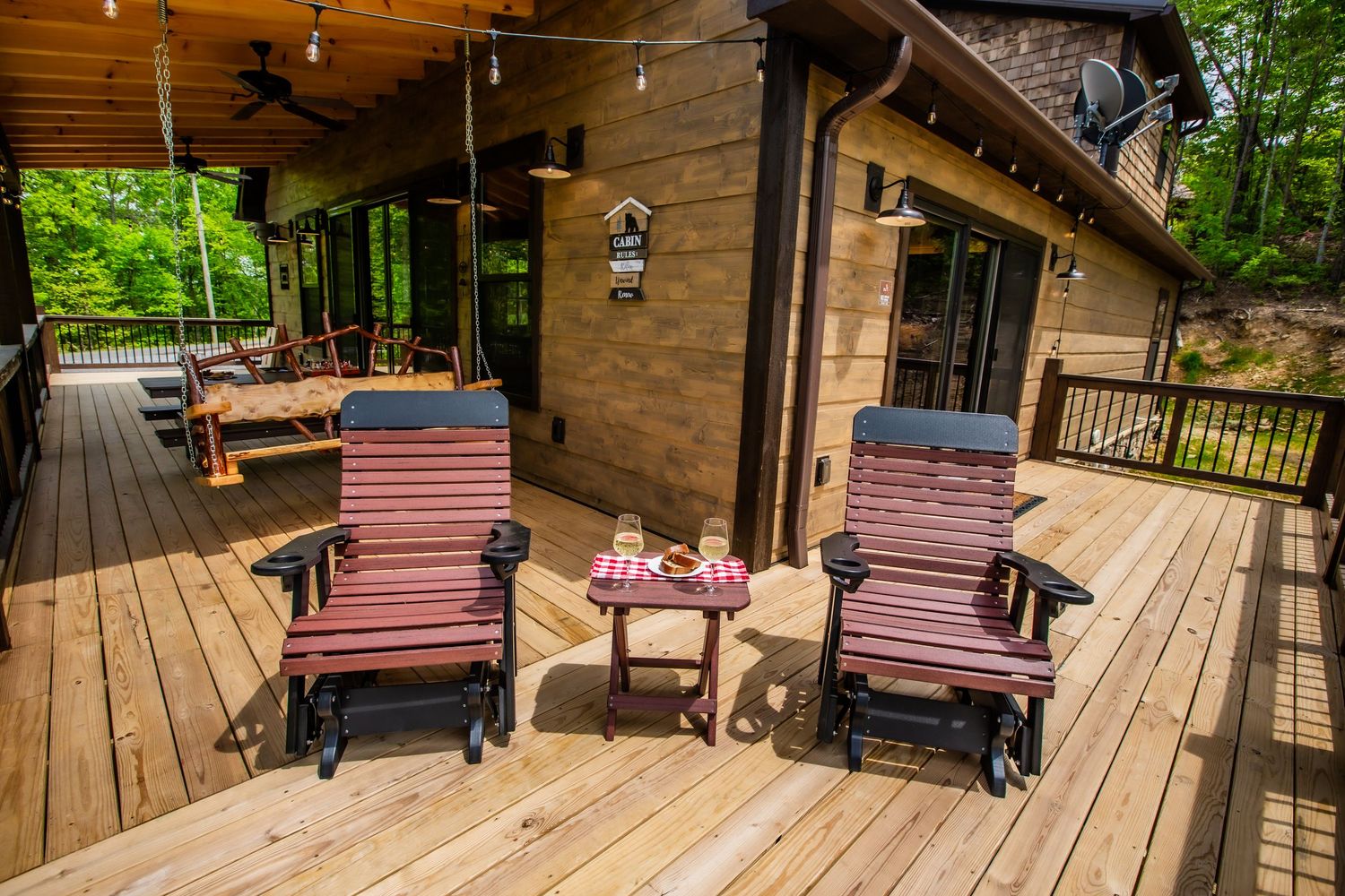 Wooden deck with two red glider chairs and small table at rustic cabin with forest view in background.