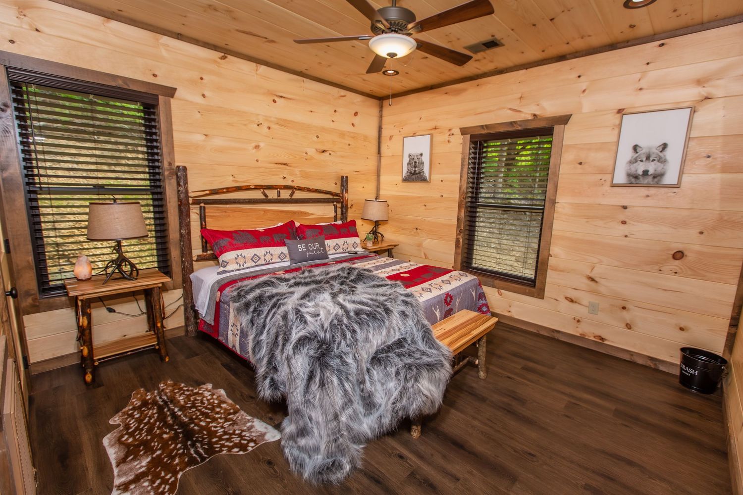 Modern log cabin bedroom interior featuring wood paneled walls, ceiling fan, and plush gray bedding.