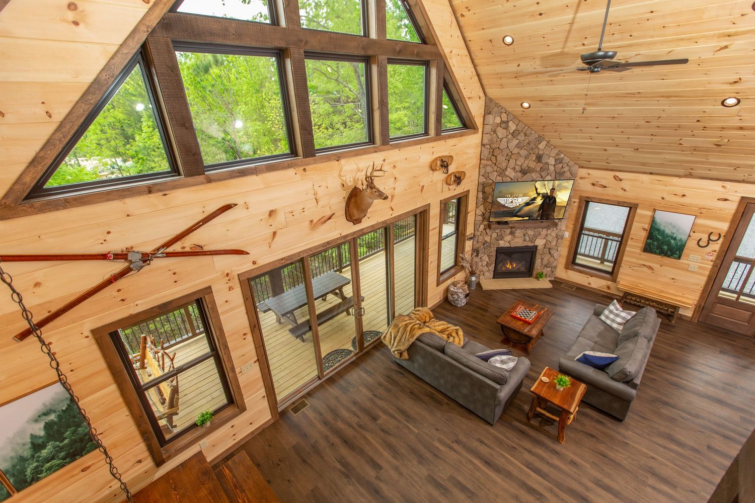 Cozy wooden cabin interior with exposed beams, vaulted ceiling, and large windows overlooking green forest views.