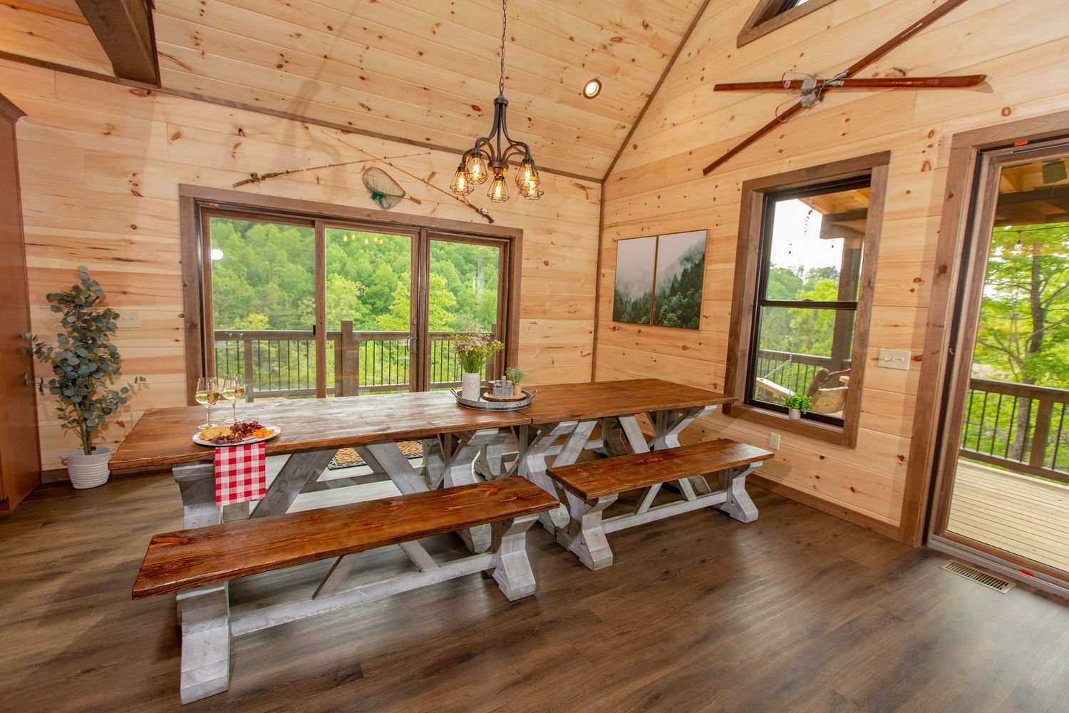 Spacious cabin interior with vaulted wood ceiling, exposed beams, and large windows letting in natural light.