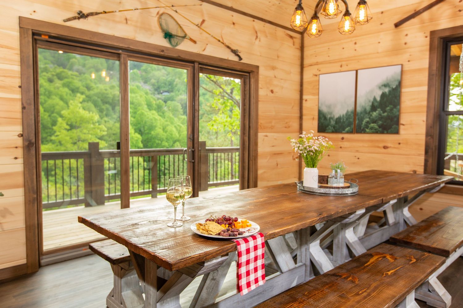 Open concept cabin dining area with wooden table and benches facing panoramic forest views through windows.