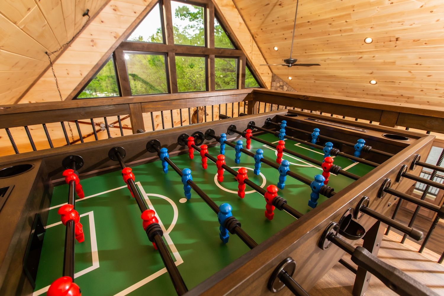 Indoor foosball tables line the walls of a wooden-paneled game room with bench seating and ceiling fans.