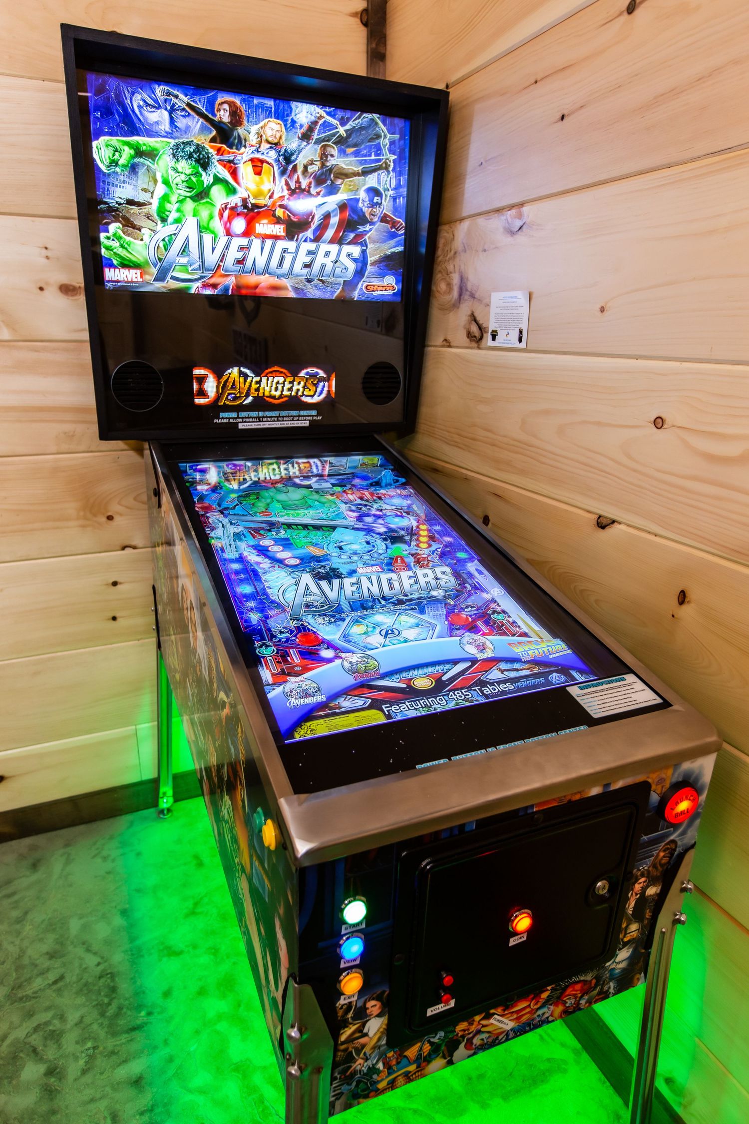Arcade game room featuring a pinball machine with colorful LED lighting and wood-paneled walls.