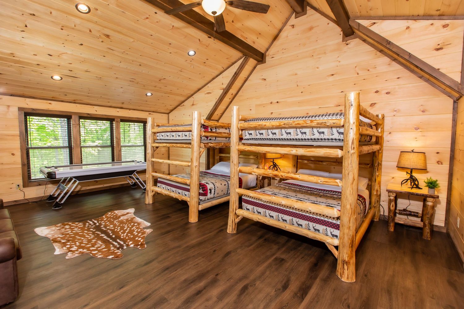 Rustic log cabin bedroom with vaulted wood ceiling, bunk beds, and warm lighting creating a cozy mountain retreat atmosphere.