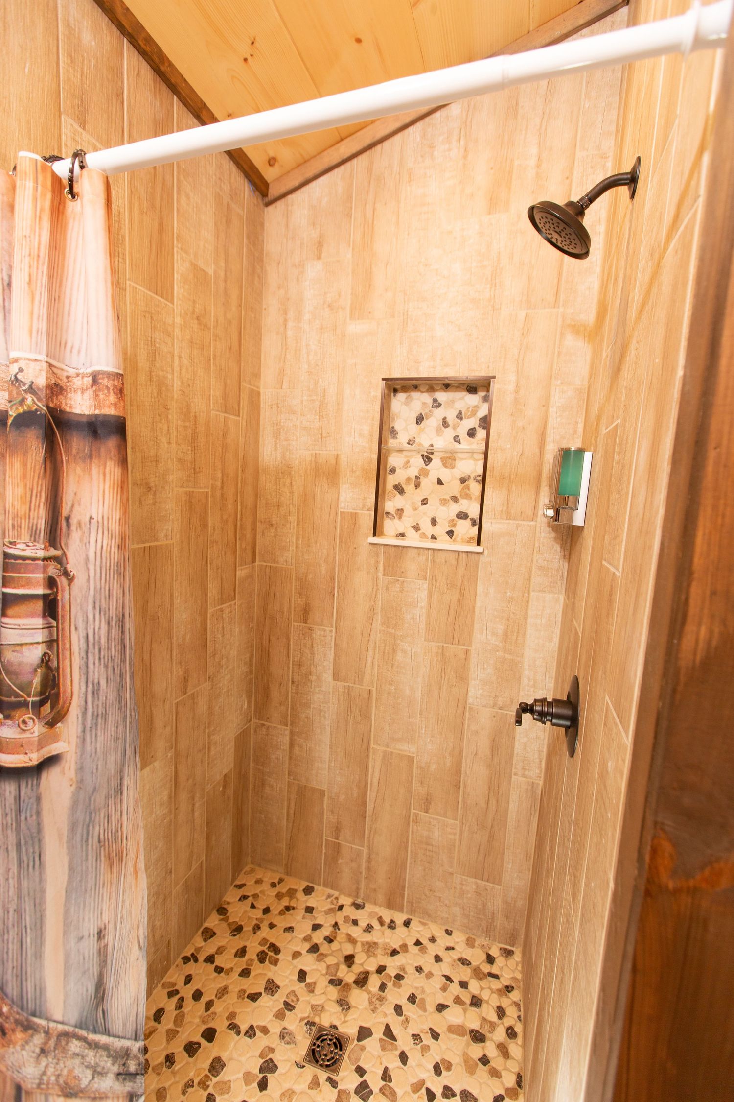 Wooden shower stall interior with tiled floor and wall-mounted showerhead in rustic bathroom setting.