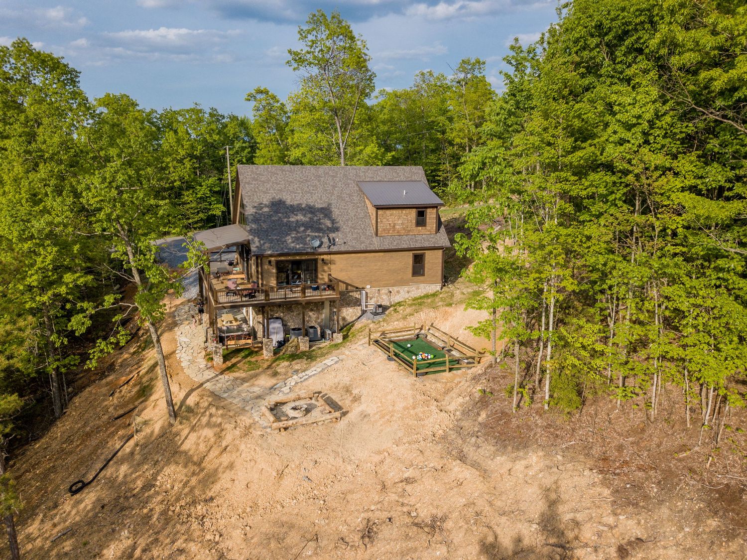 Aerial view of a burnt house on a hillside with surrounding forest and blue sky in the background.