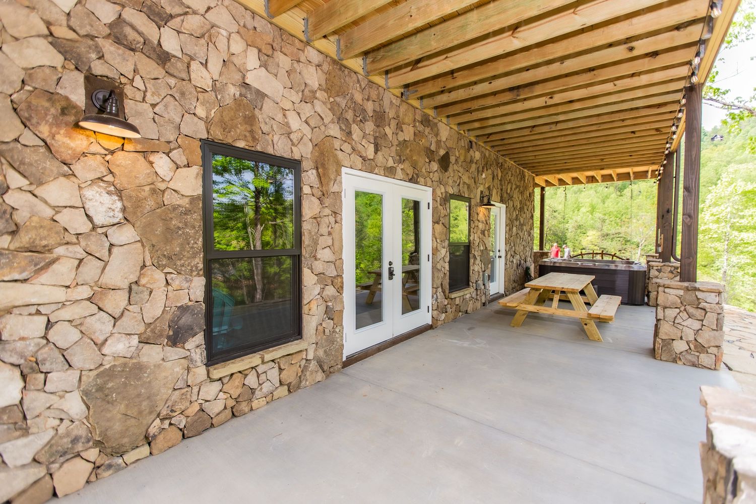 Stone-walled covered patio with exposed wooden beams and outdoor seating area.