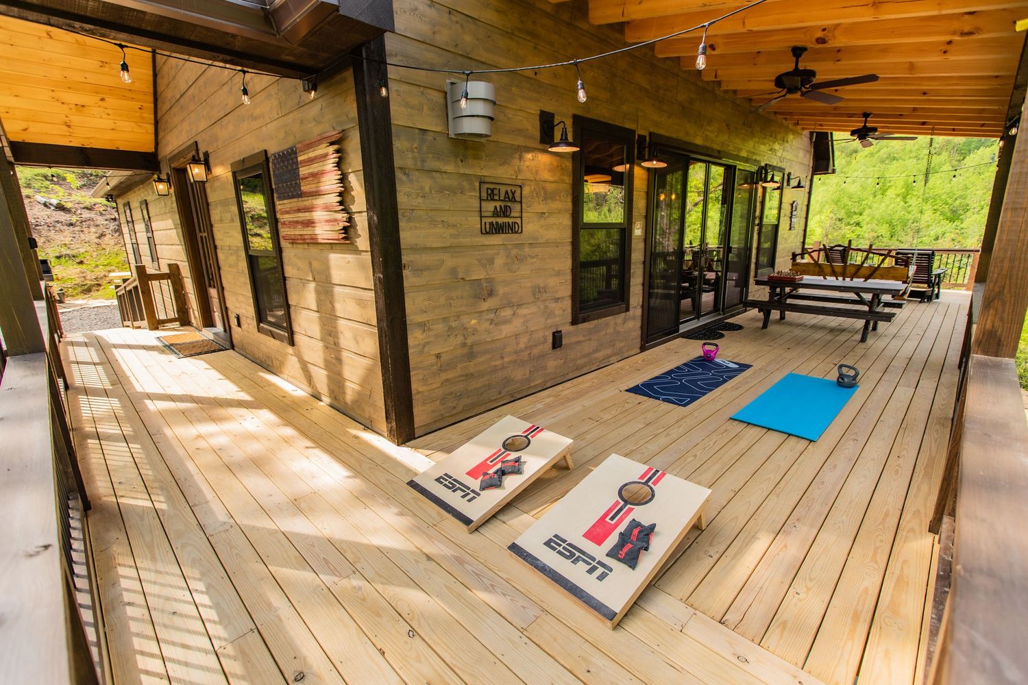 Rustic wooden deck with rocking chairs and outdoor seating extends along a cabin in a peaceful forest setting.