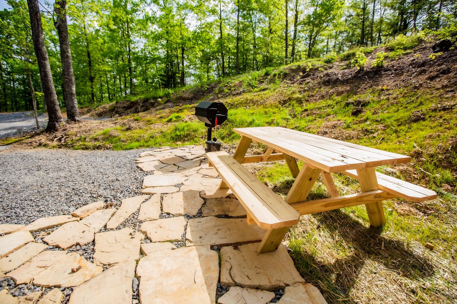 Stone pathway leading to a wooden picnic area surrounded by lush green forest and mountain views.