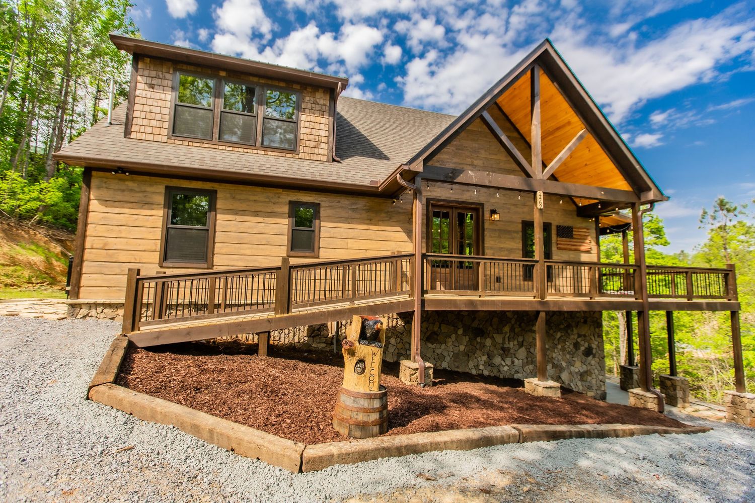 Exterior view of large luxury log cabin with wraparound porch nestled in wooded mountainside.