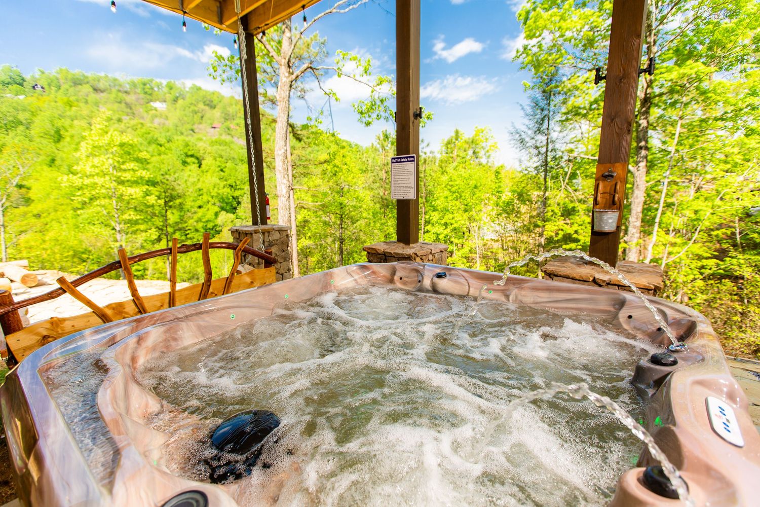 Outdoor hot tub with bubbling water on wooden deck surrounded by forest scenery and mountain views.