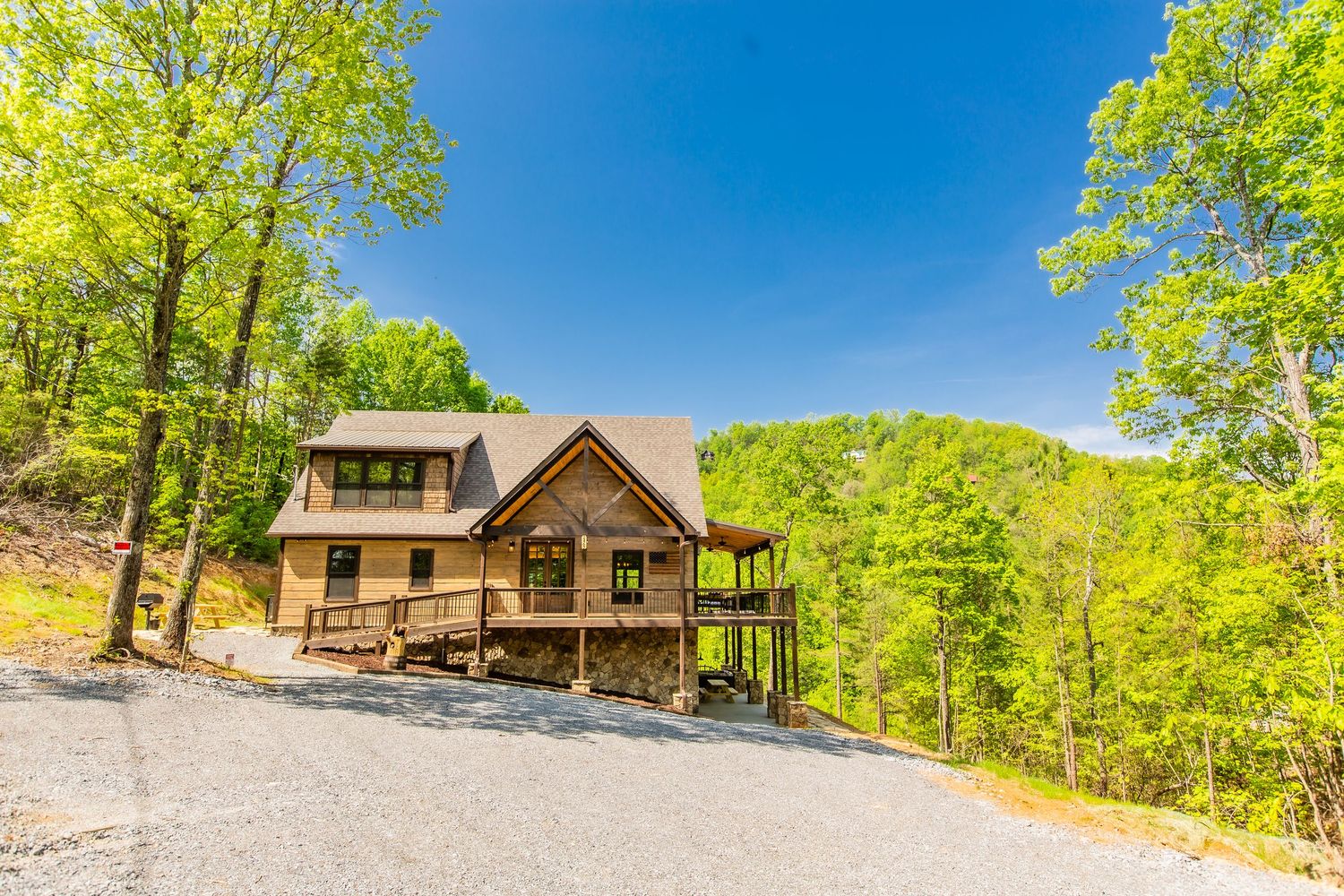 Panoramic view of rustic wooden cabins nestled among lush green trees under bright blue summer sky.