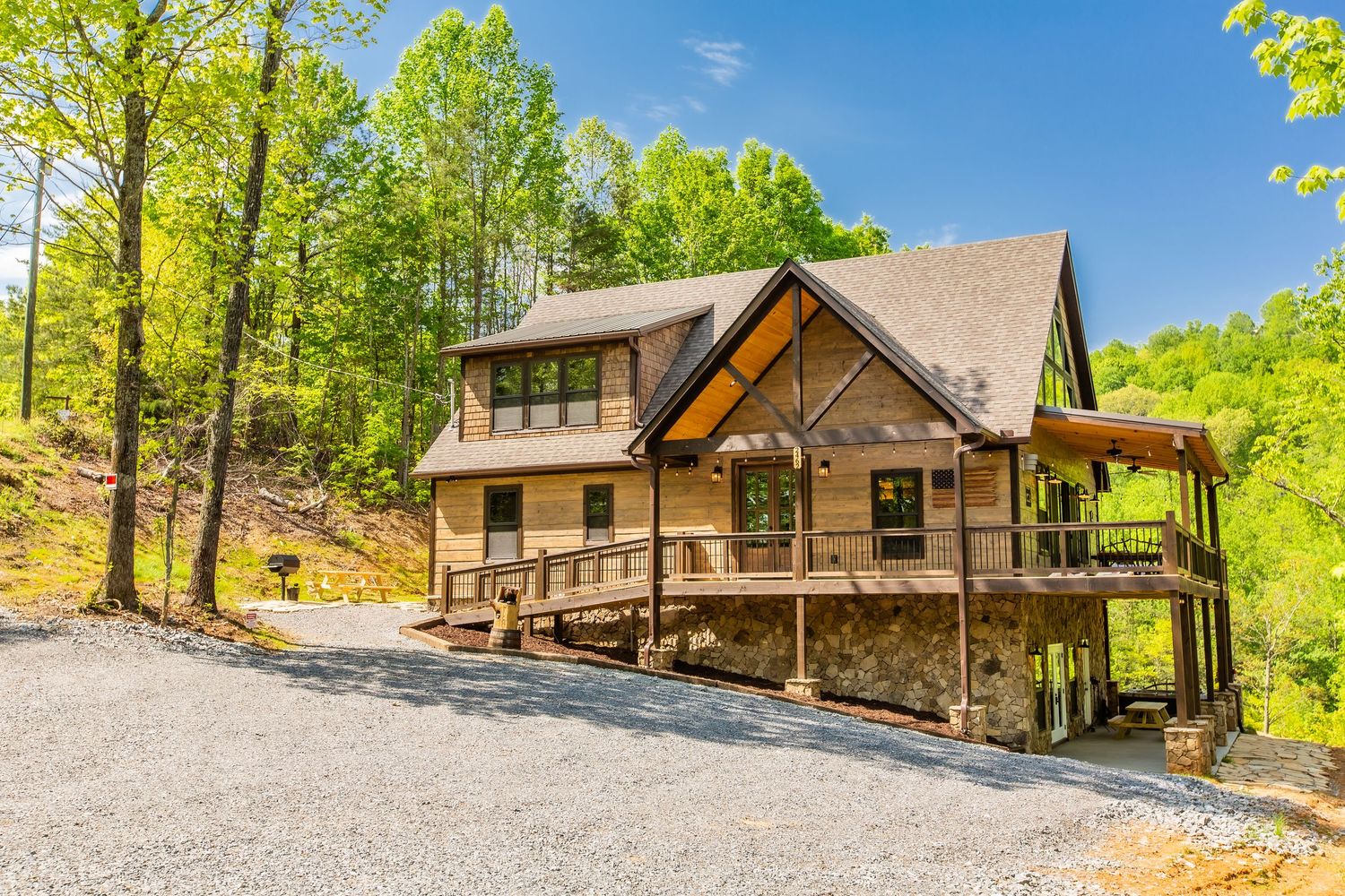 Modern wooden cabin with stone accents nestled among green trees on a sunny day with multiple exterior views.