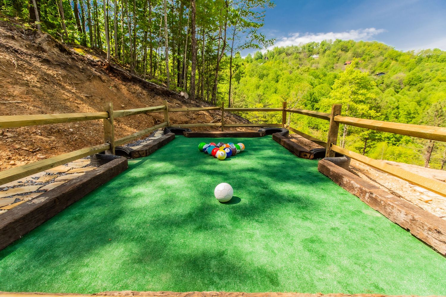 Series of putting green holes on an outdoor deck surrounded by forest scenery.