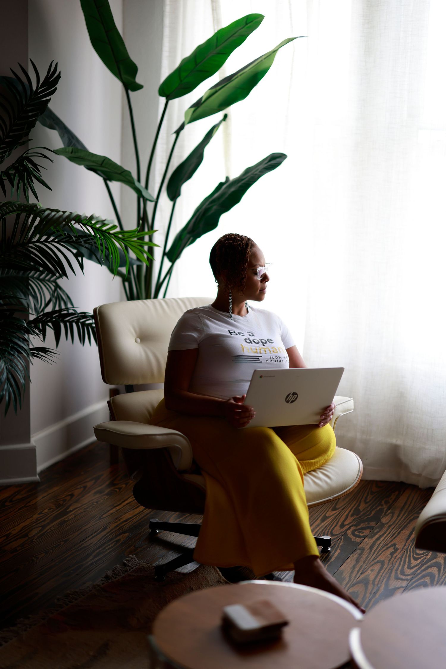 Person relaxes in white chair near indoor plants in modern living space with hardwood flooring and natural light.