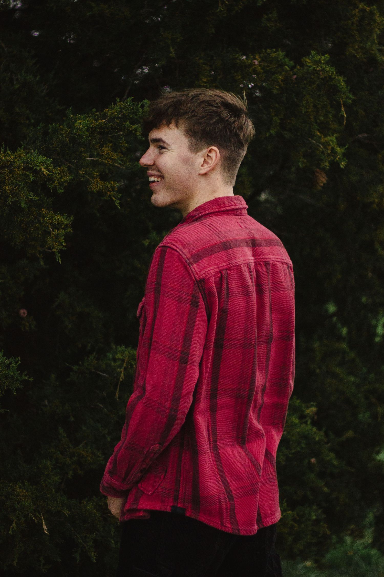 Side profile of person wearing red plaid flannel shirt against dark foliage.